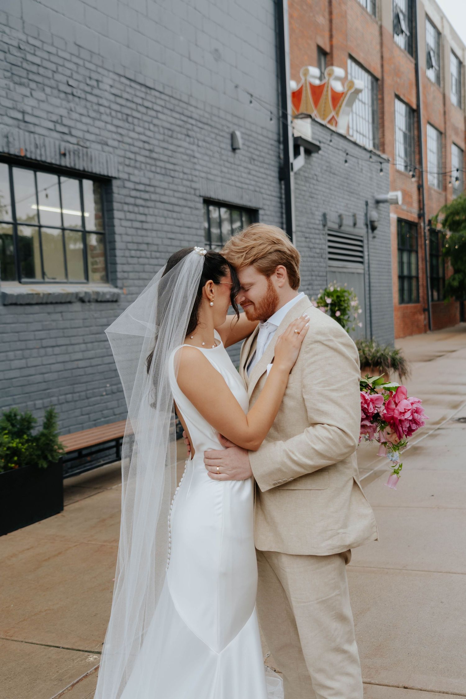 A romantic wedding photoshoot against an industrial brick wall backdrop with pink floral accents.