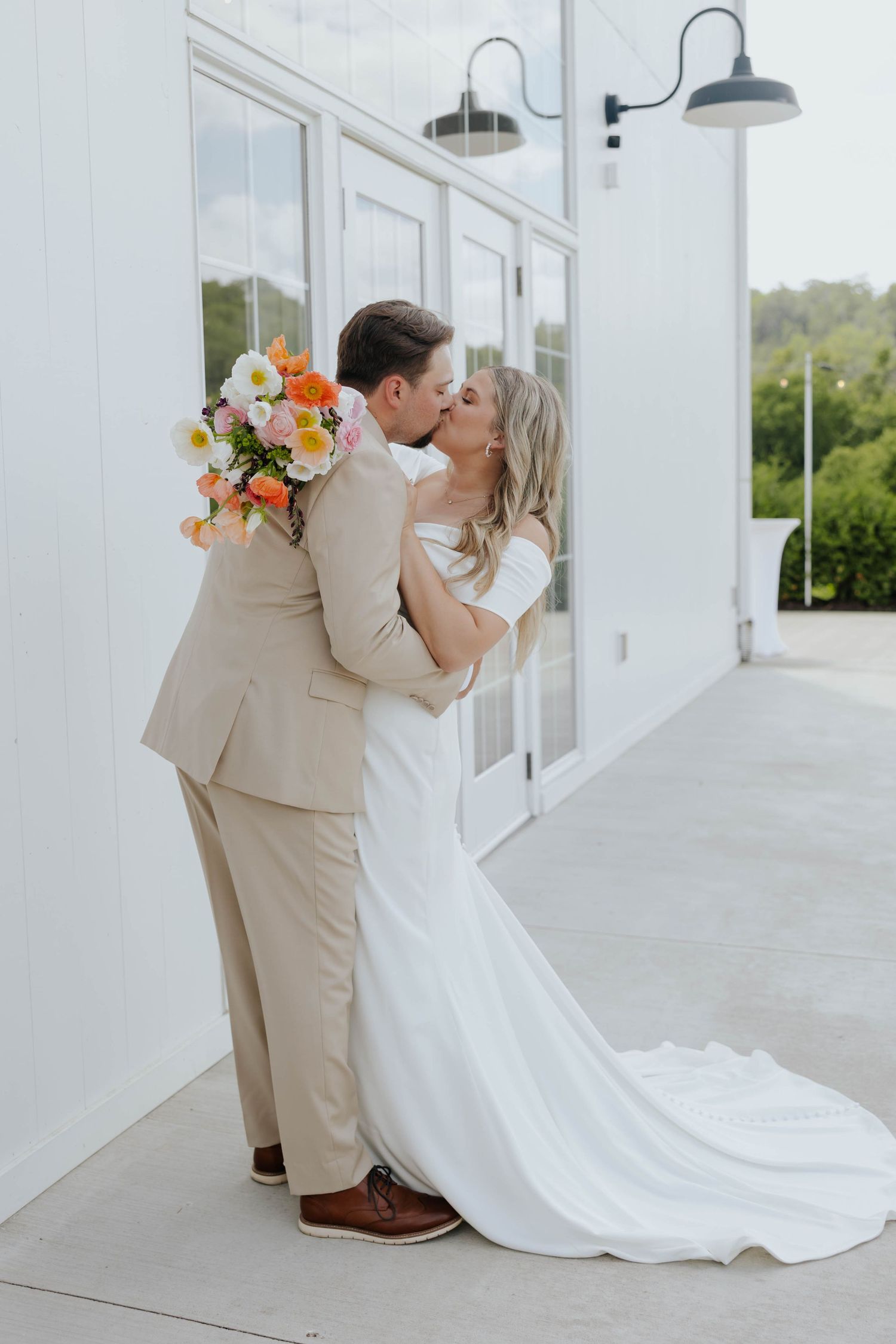 Romantic wedding couple shares intimate kisses along a white columned porch with floral bouquet.