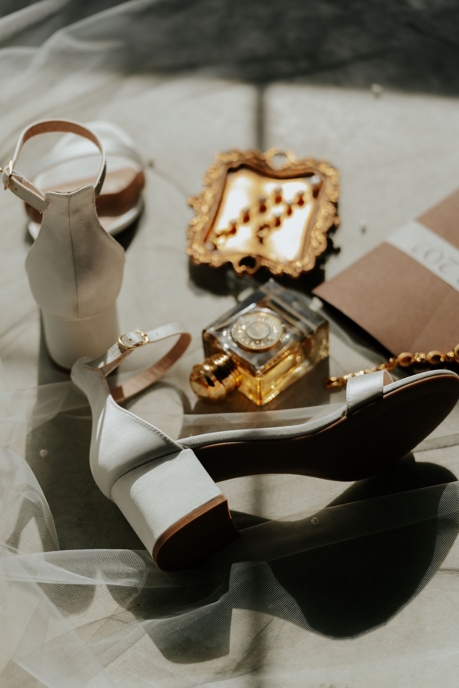 White bridal heels, gold perfume bottle, ornate mirror, and accessories arranged on a soft fabric surface.