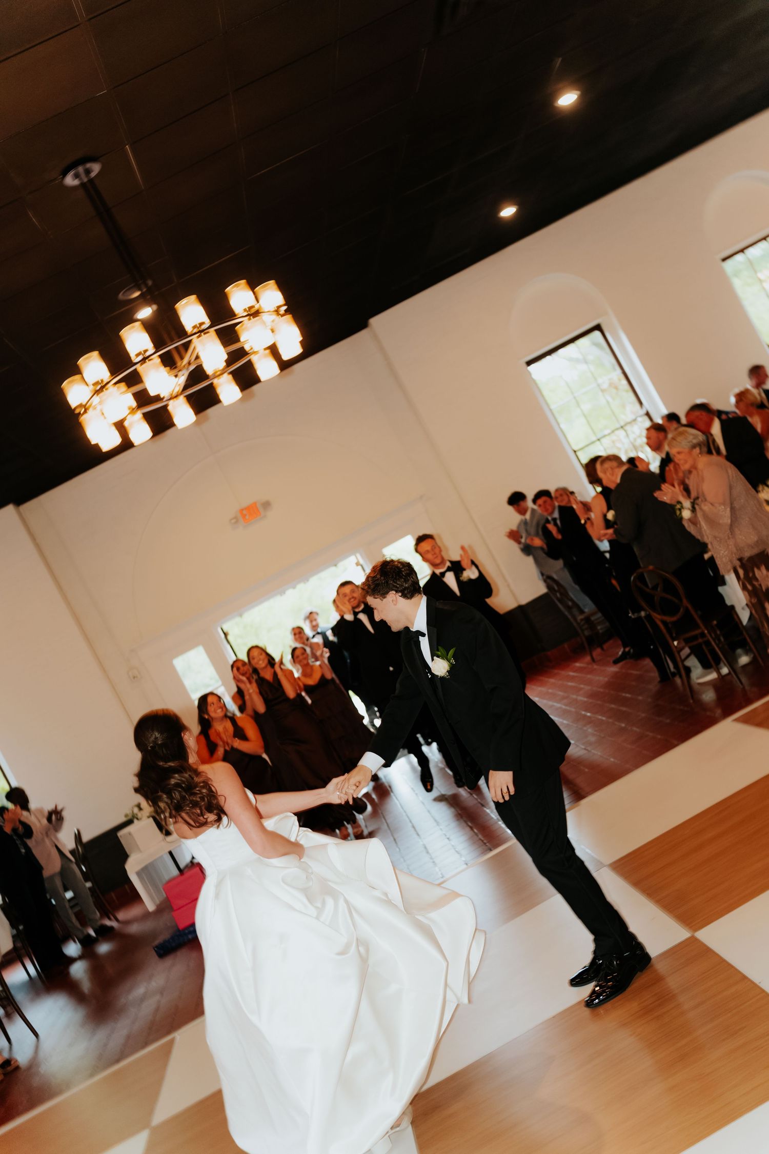 Bride and groom share their first dance on a checkered floor at an elegant wedding reception.