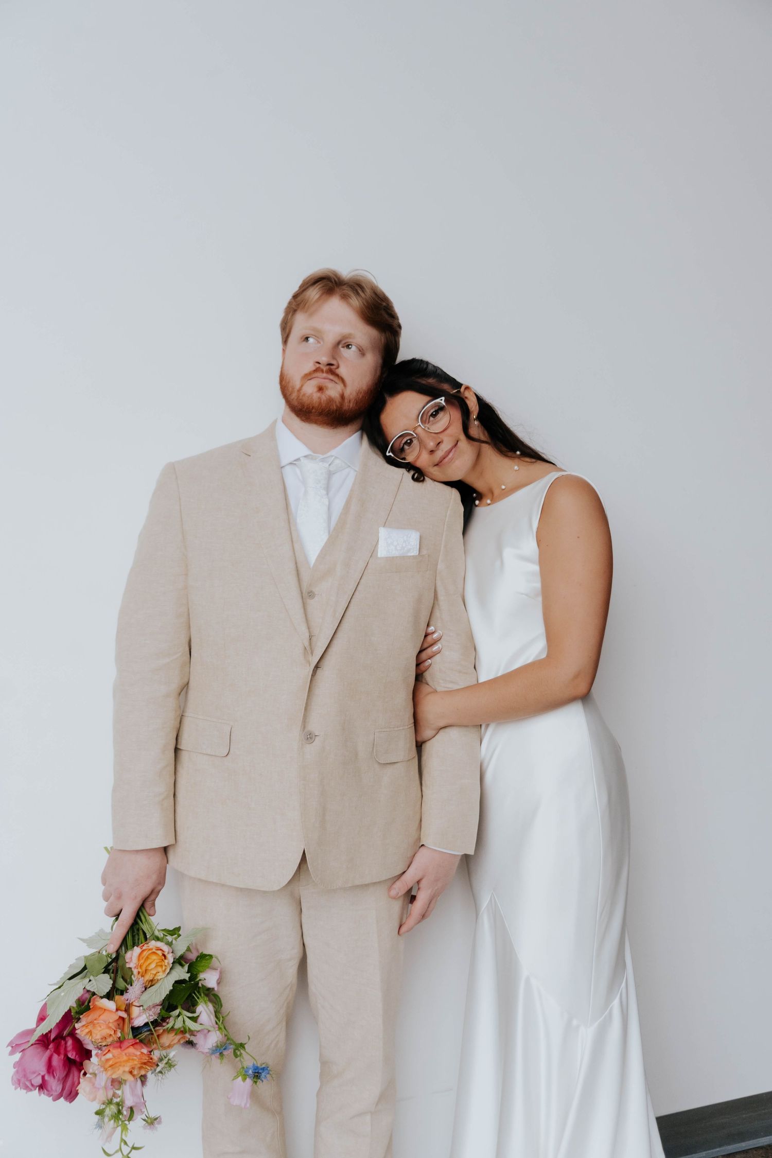 A couple in wedding attire shares intimate moments against a minimalist white backdrop.