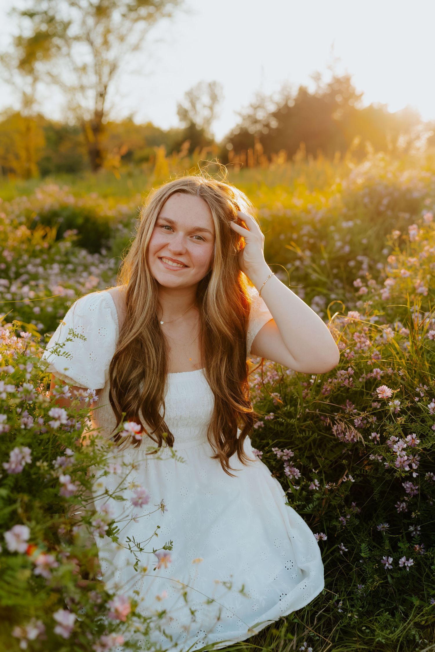Young woman in white dress smiling in a wildflower field during golden hour sunset.
