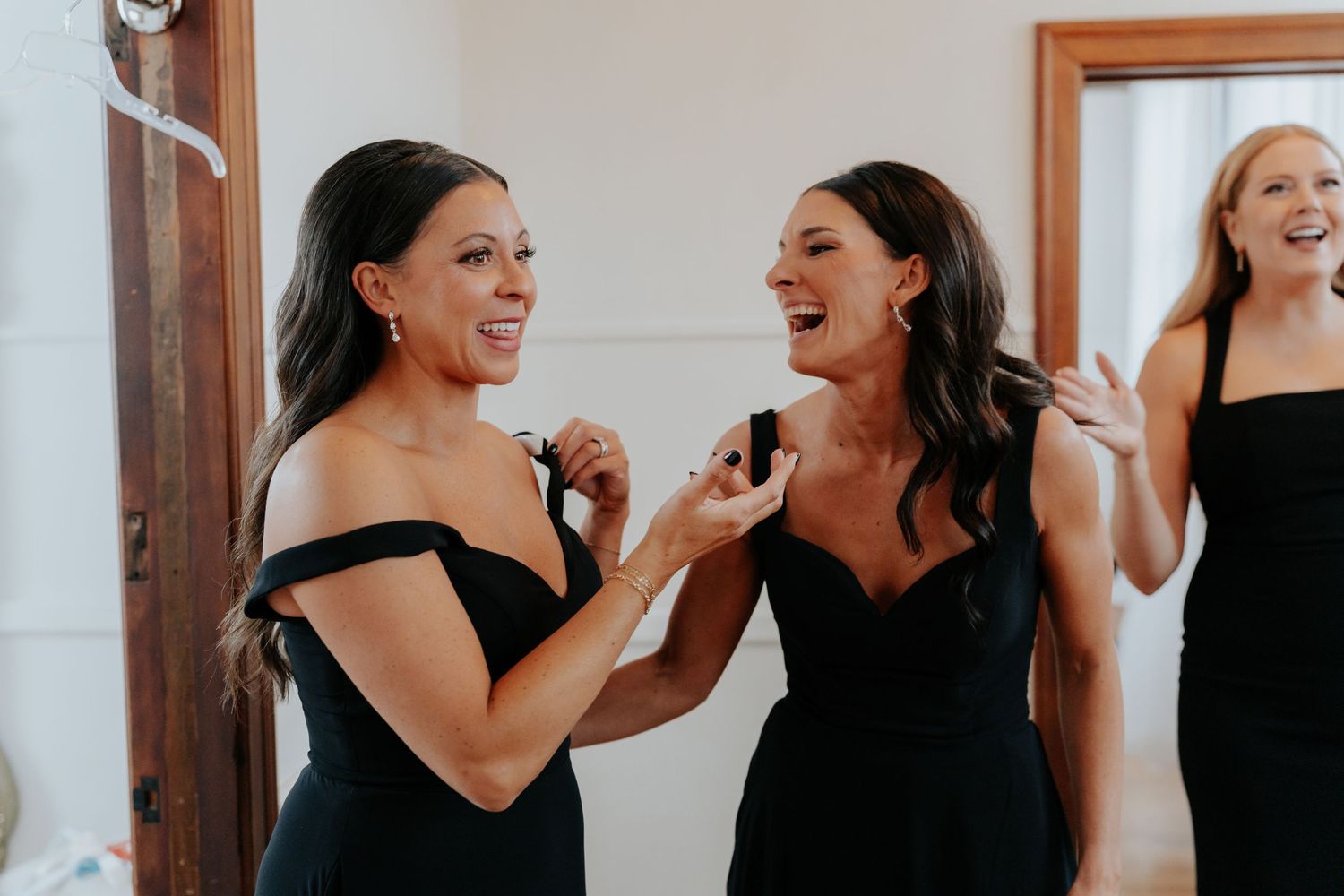 Bridesmaids in black off-shoulder dresses laughing and sharing a joyful moment together before a wedding ceremony.