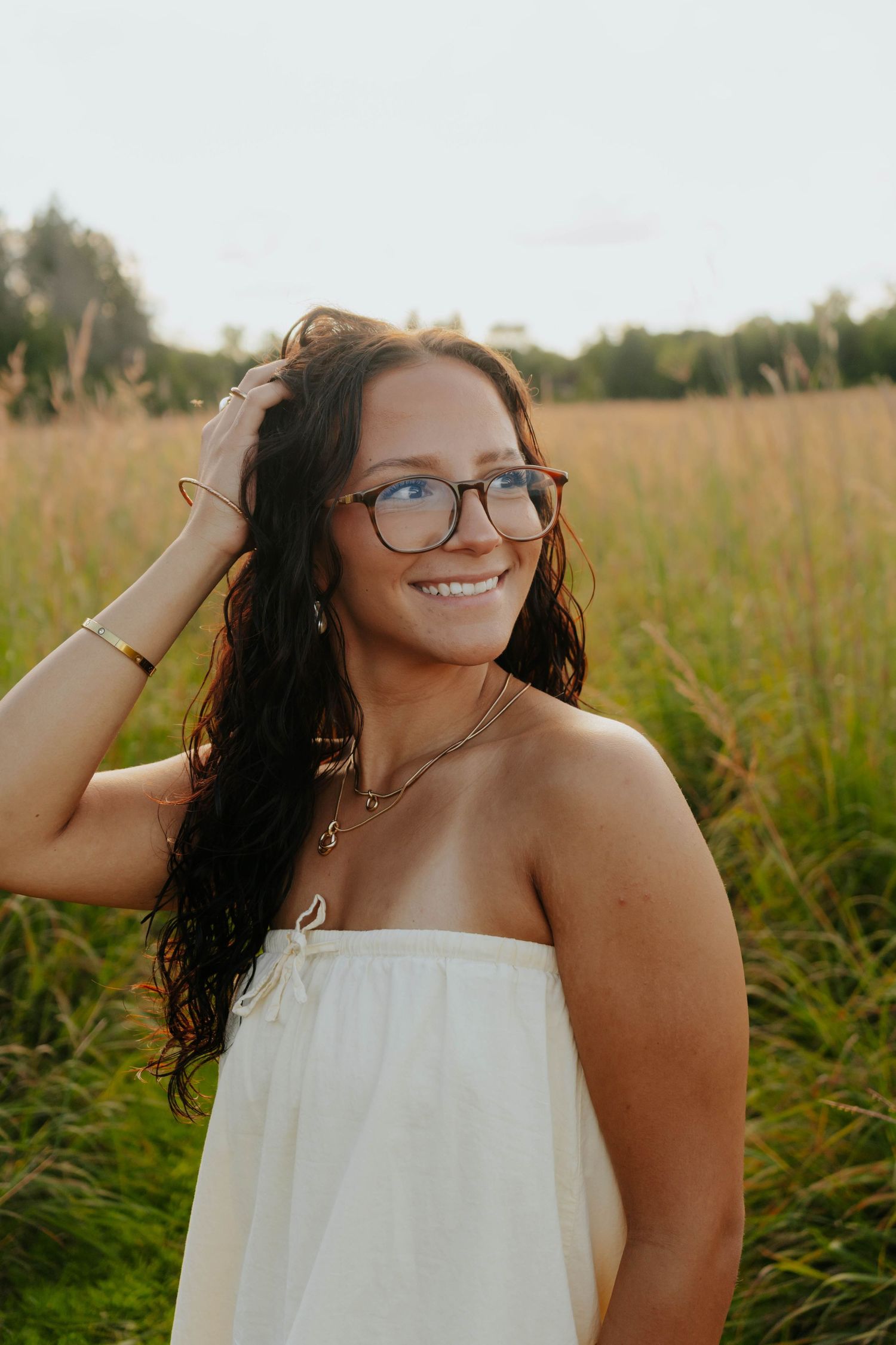 Person in white dress smiles while posing in a natural field setting.