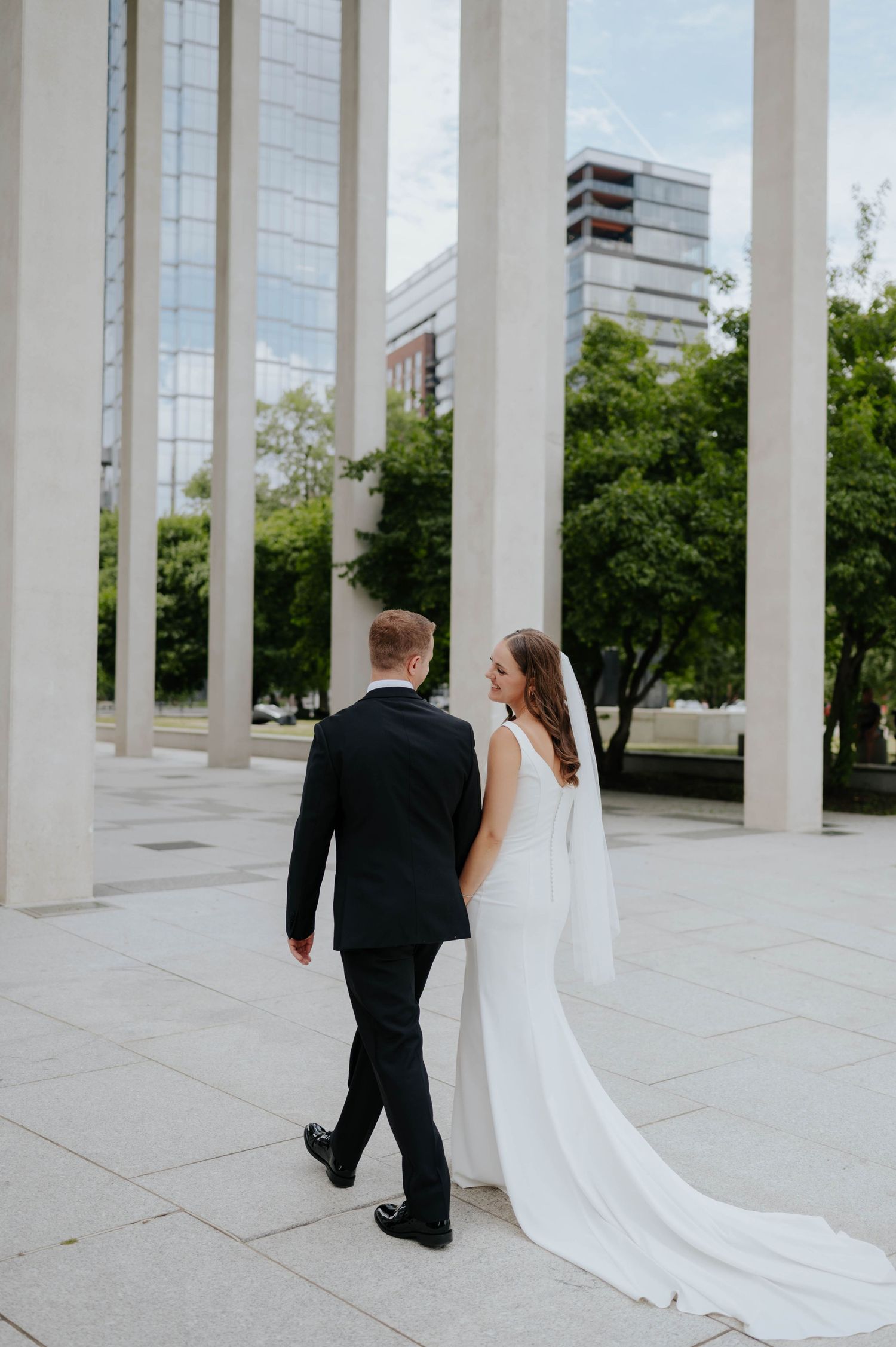 Elegant wedding portraits taken between white architectural columns in an urban setting.