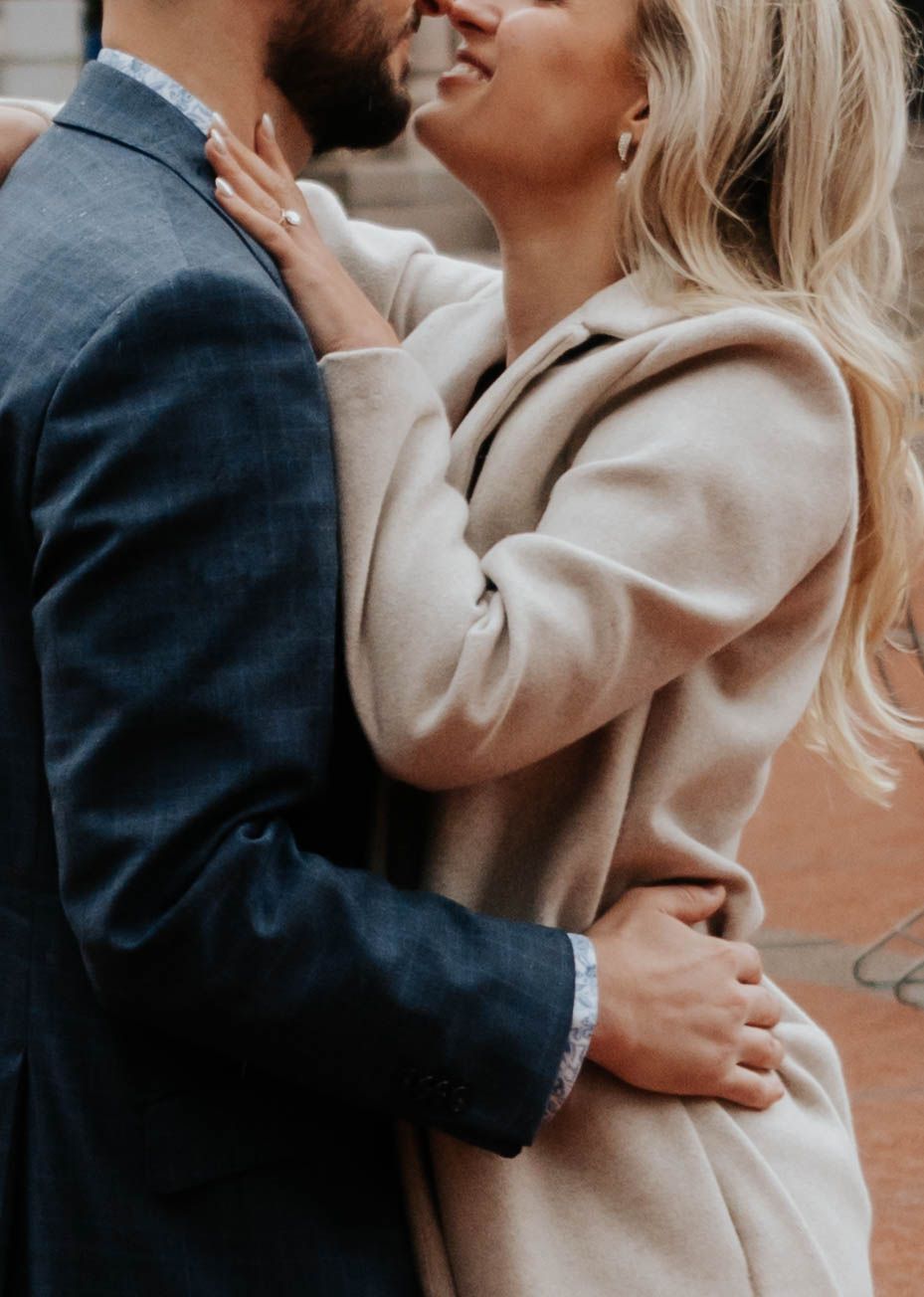 A romantic couple embraces intimately, with the person wearing a beige sweater and the other in a dark suit jacket.