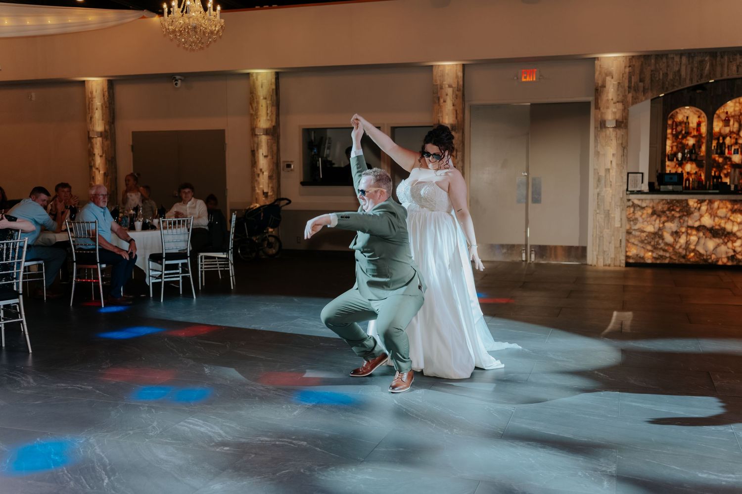 Bride and groom share a lively first dance at elegant wedding reception venue with decorative lighting.