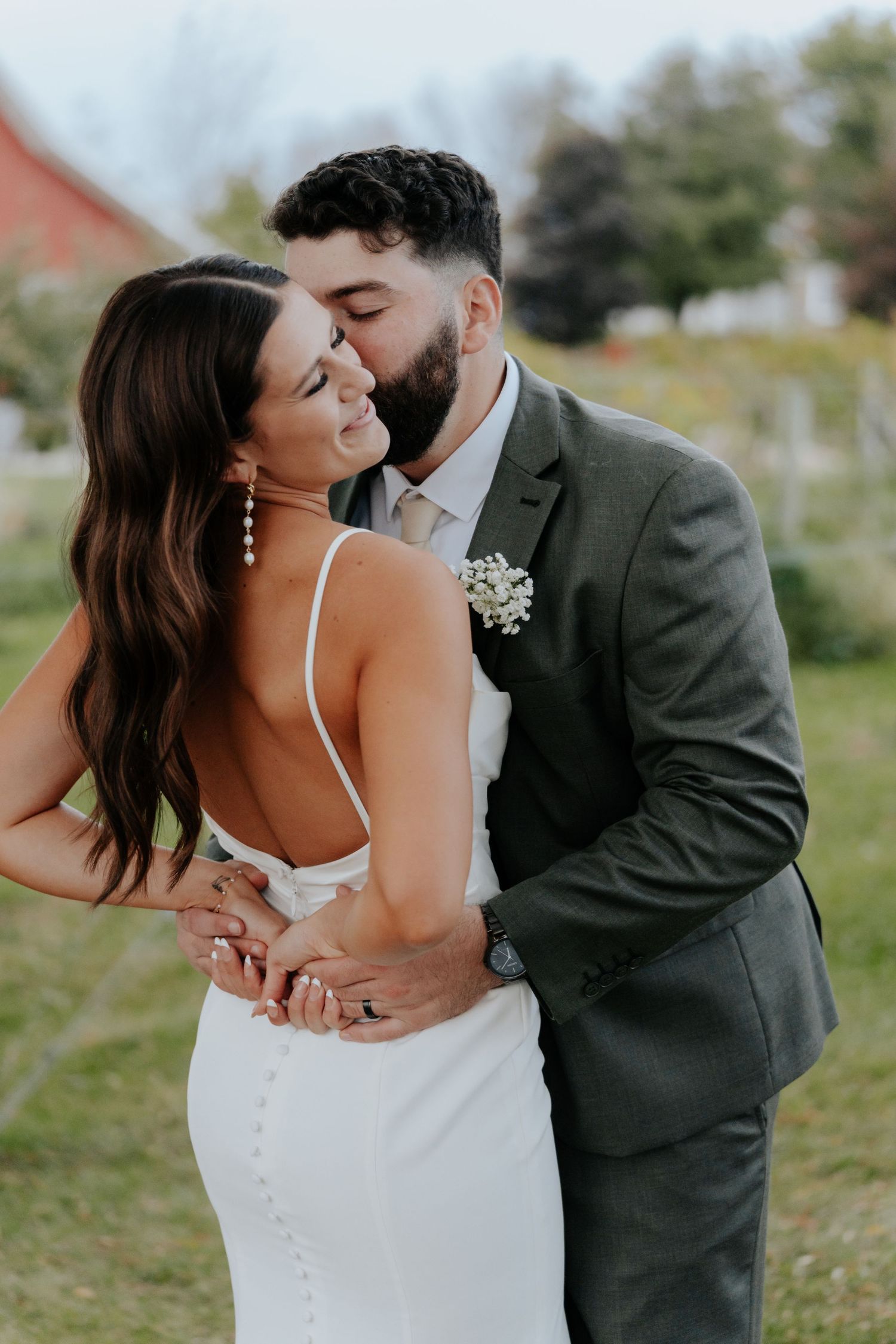 A romantic wedding moment captured outdoors with the couple embracing in front of a rustic red barn.