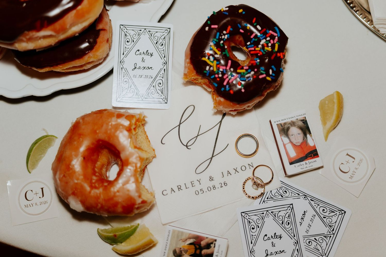 Wedding reception table with glazed and chocolate donuts, gold rings, Polaroid photos, and custom Carley & Jaxon branded cards.