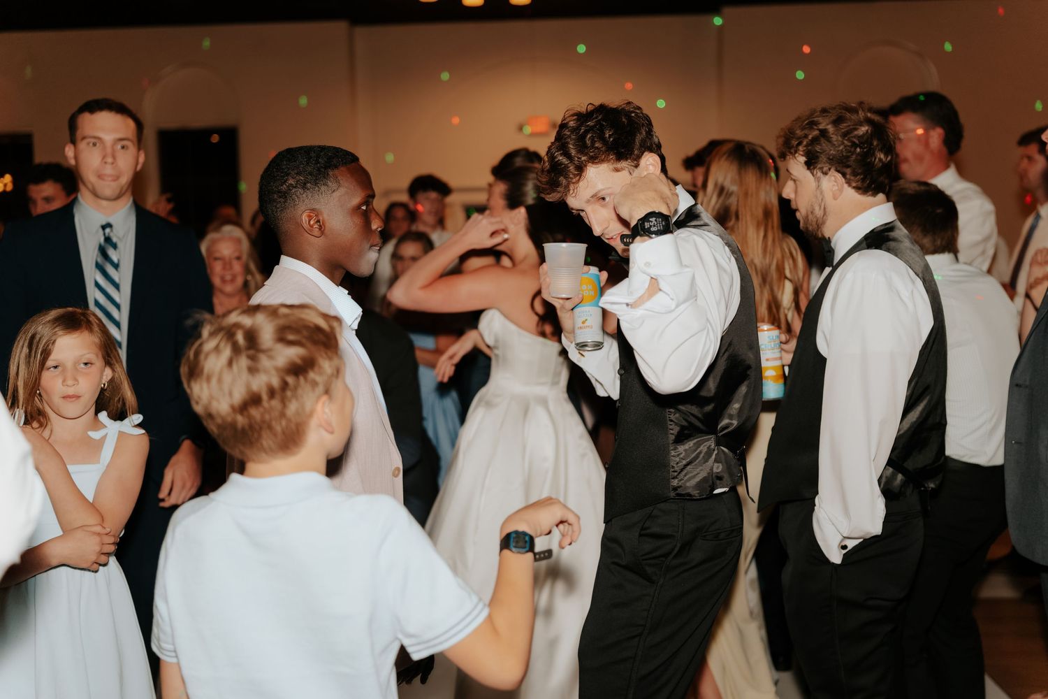 Guests dancing joyfully at a wedding reception, including children and adults in formal attire on a crowded dance floor.