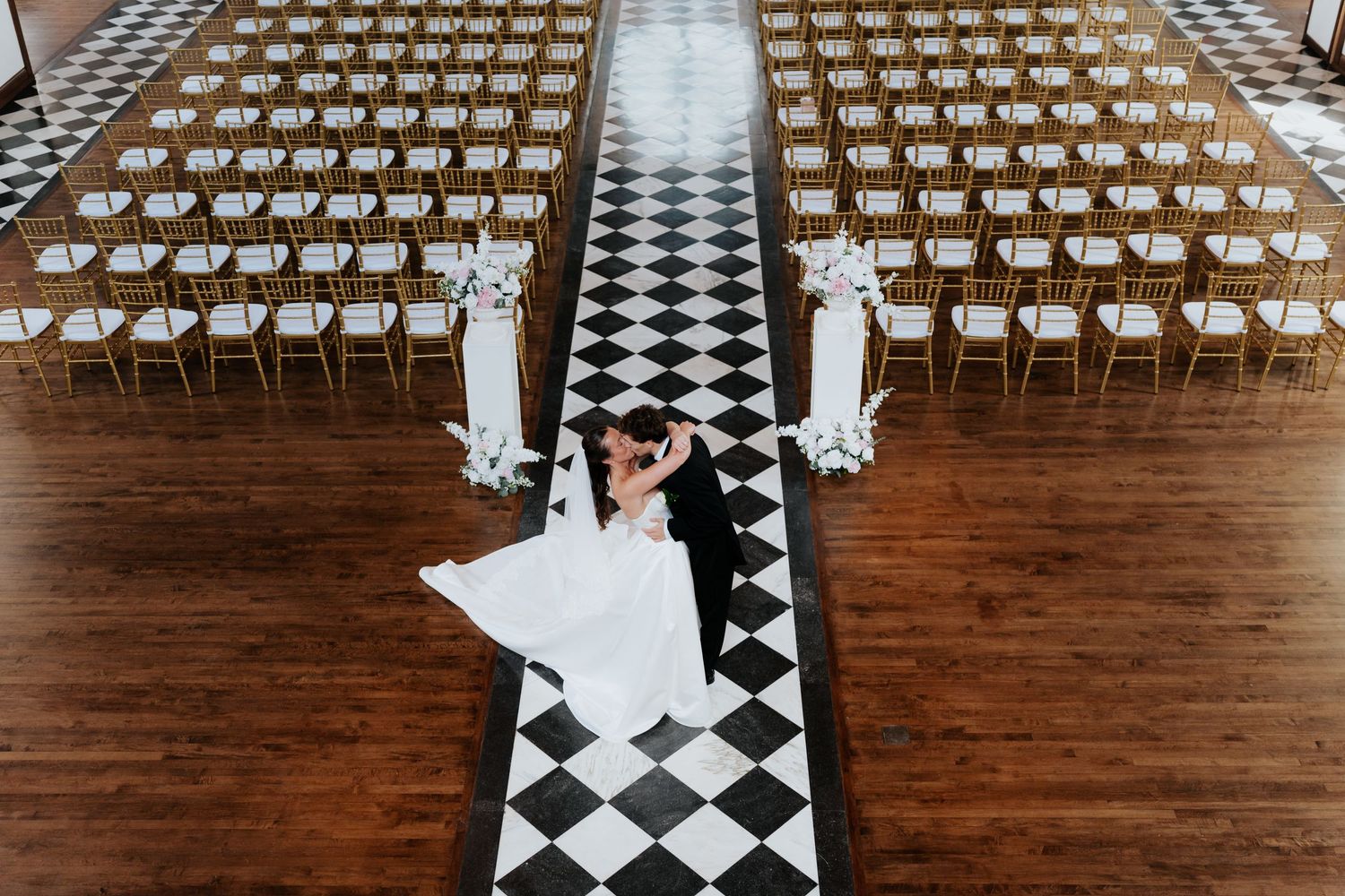 Bride and groom share first dance on black and white checkered aisle in elegant wedding ceremony venue.
