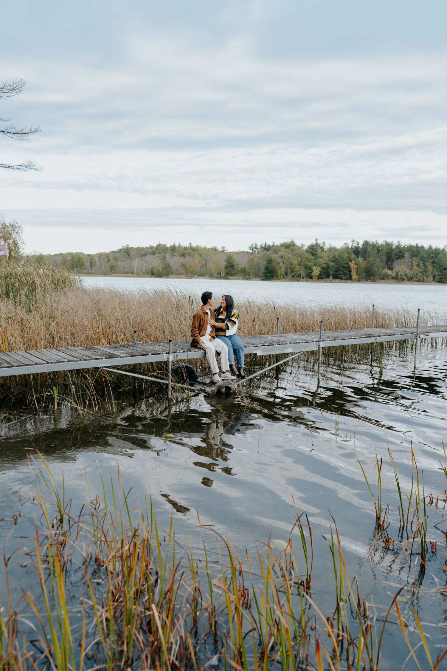 Couple sharing romantic moment on wooden dock surrounded by lake reeds and calm waters.
