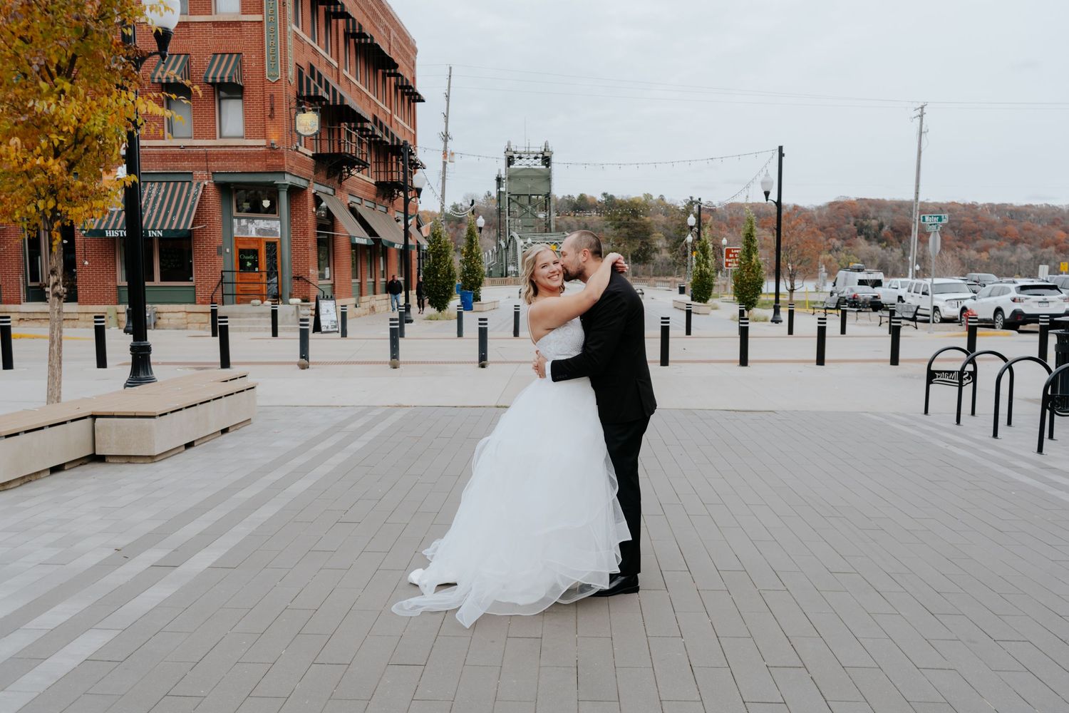 Wedding couple walking and dancing on urban sidewalk with brick buildings in background.