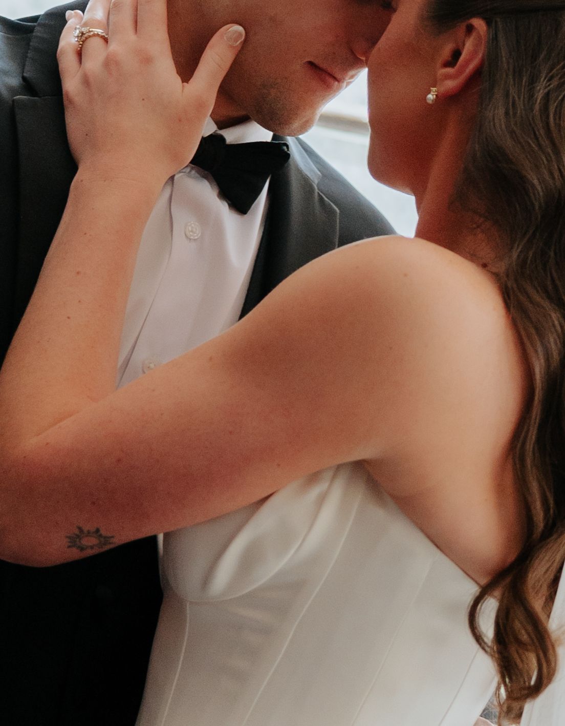 A bride and groom share a romantic moment, the bride in a white gown and groom in a black tuxedo with bow tie.