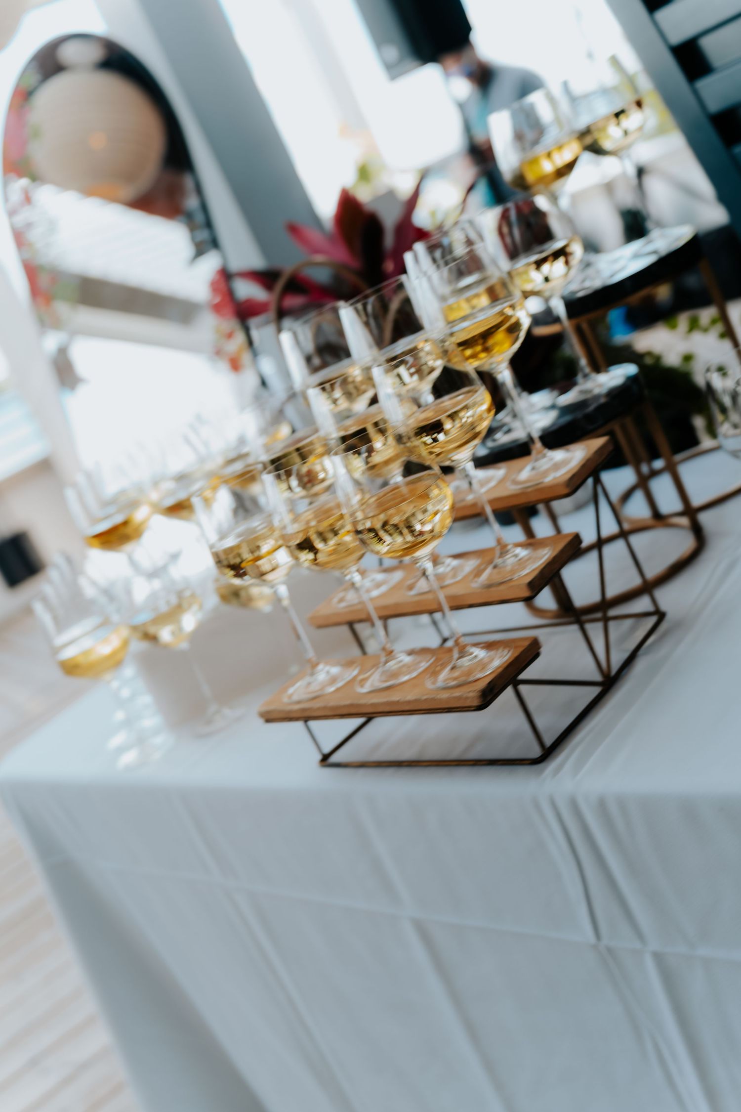 Elegant wine tasting setup with rows of white wine glasses on wooden stands atop a white tablecloth.