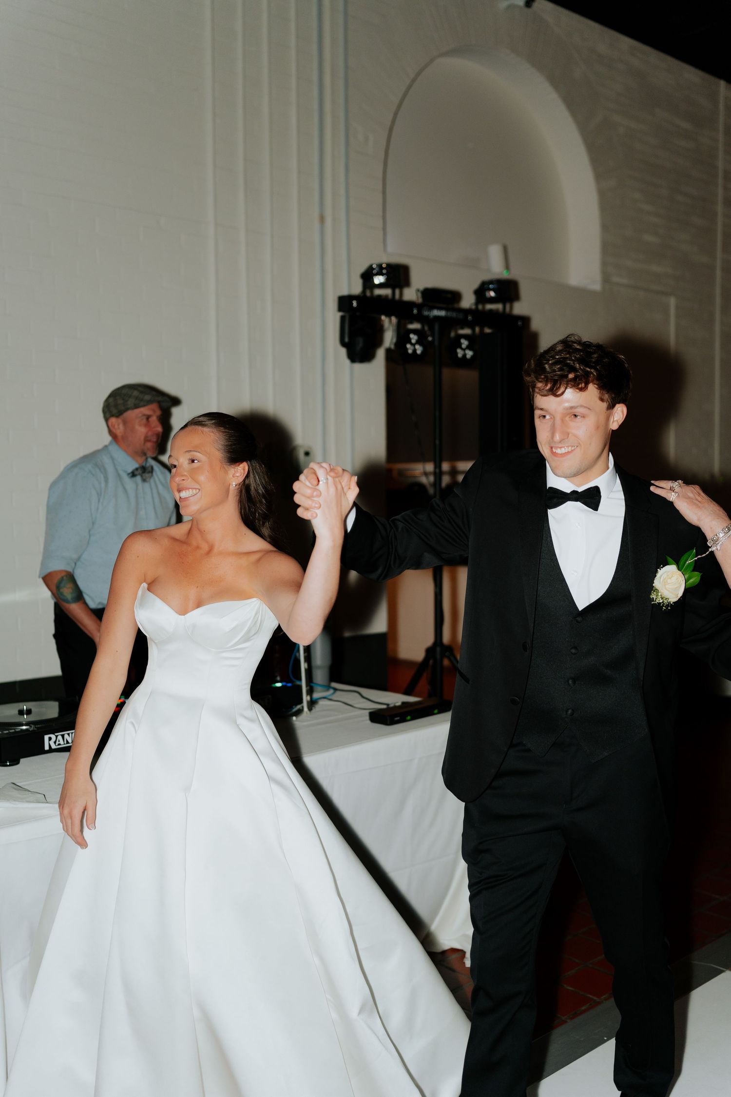 Smiling bride and groom hold hands during their first dance at a wedding reception.
