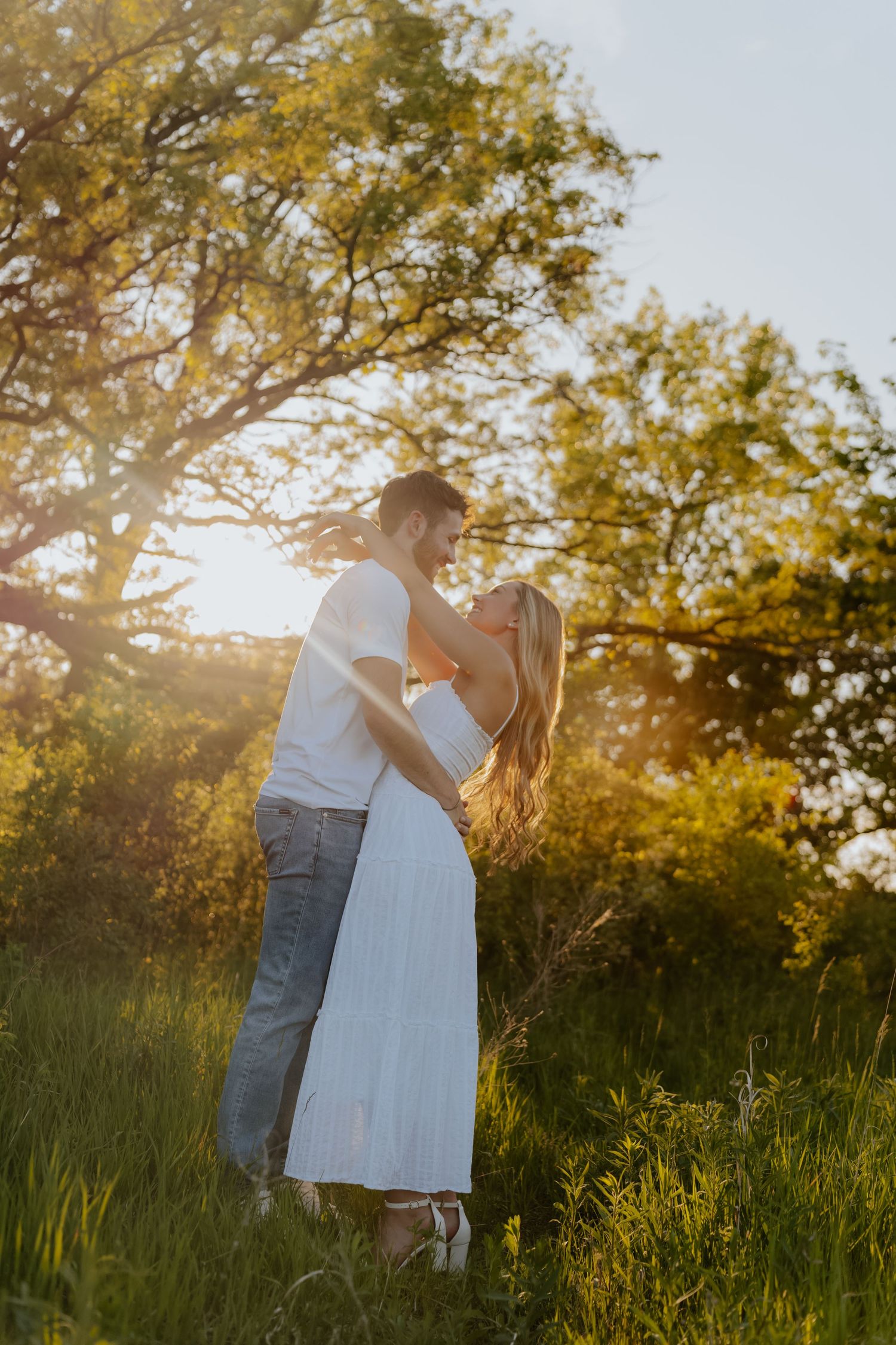 Romantic couple embracing and almost kissing in a sunlit field with warm golden hour light behind them.