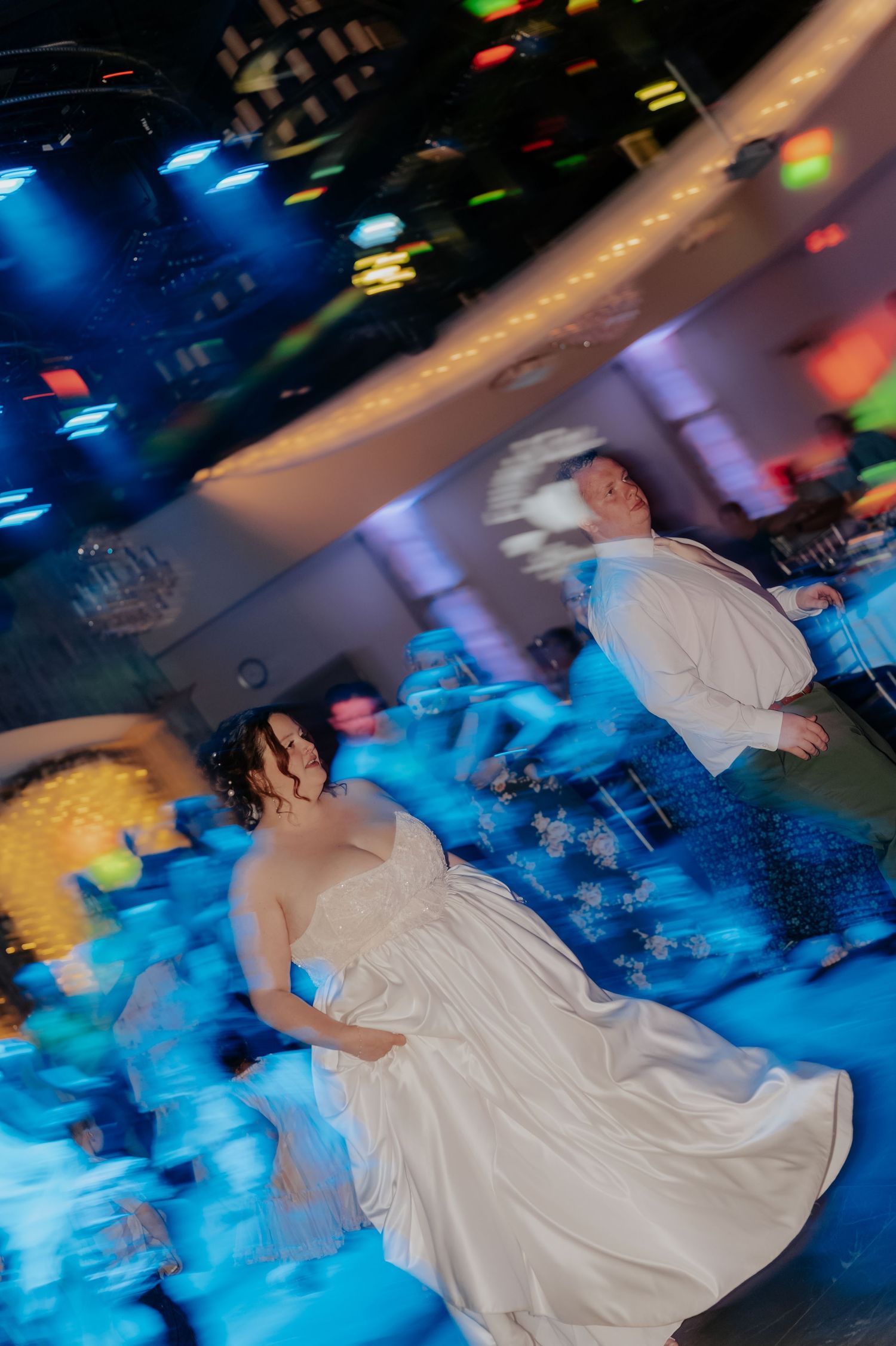 Bride and groom share first dance with colorful disco lights creating motion blur effect.