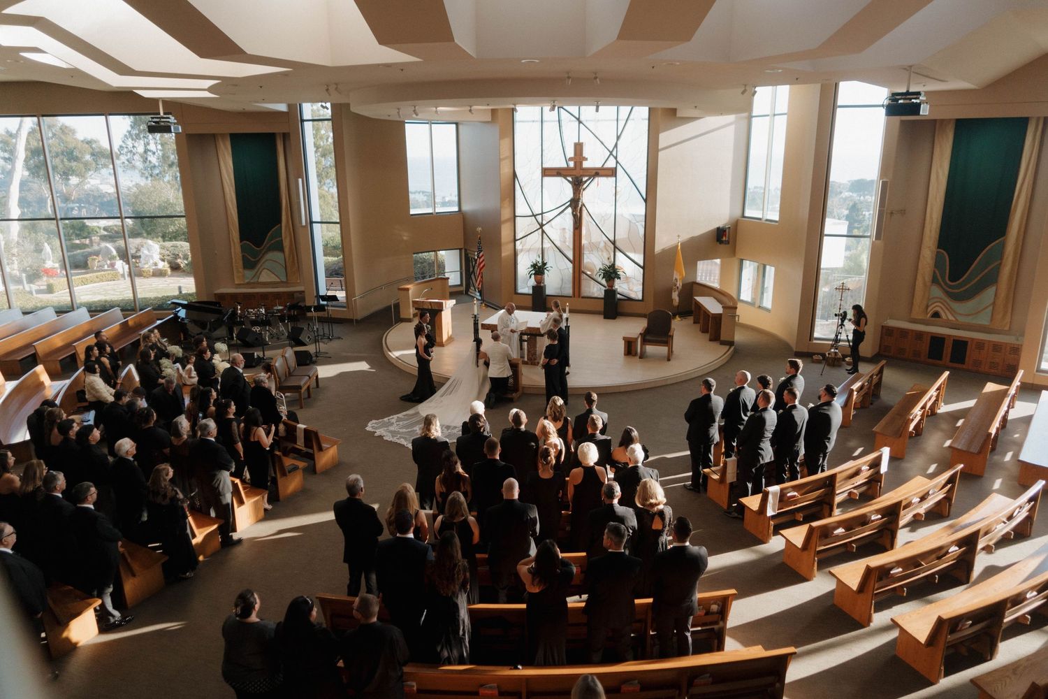 Wedding ceremony in modern church with large windows and gathered guests.