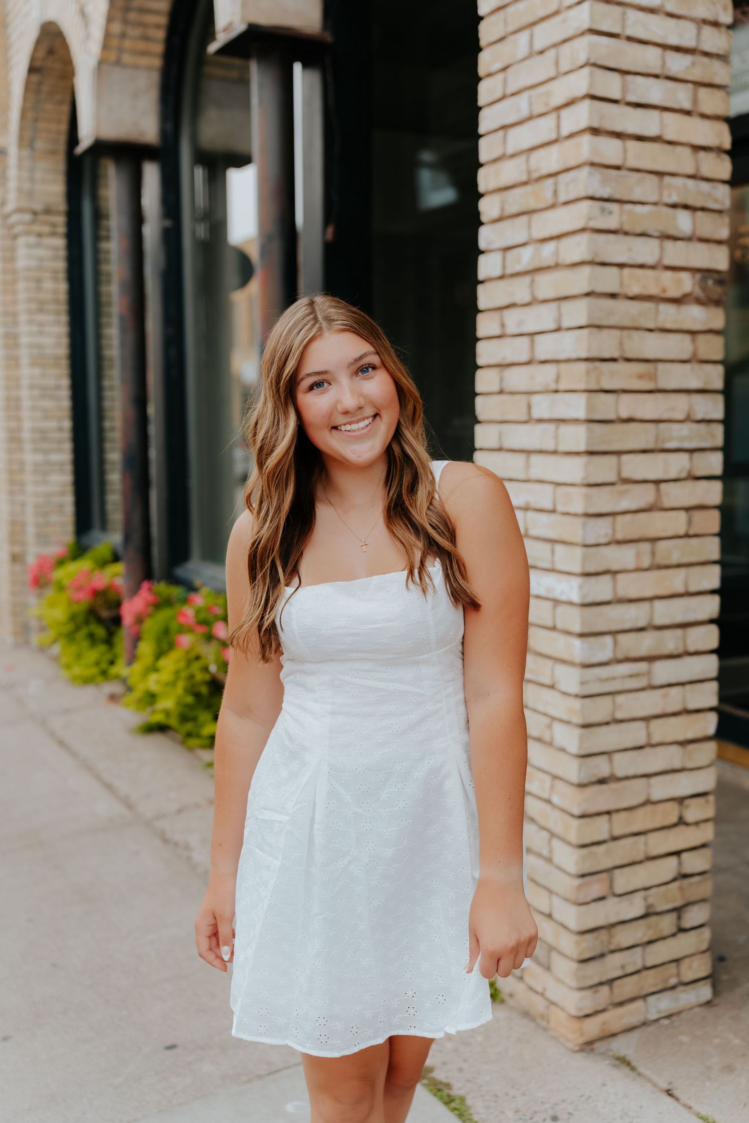 Young woman in white sundress smiling outdoors near brick building on sunny day.