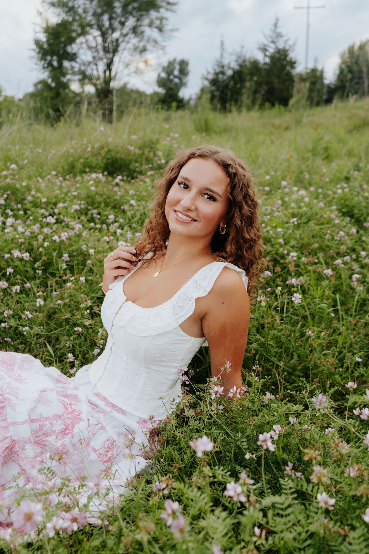 A person in a white dress poses joyfully in a summer meadow filled with delicate wildflowers and tall grass.