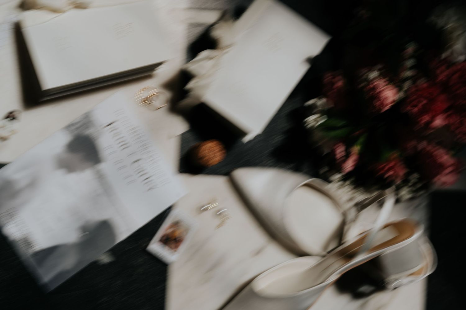 Blurred overhead view of elegant wedding stationery, menus, and floral arrangements on a dark table.
