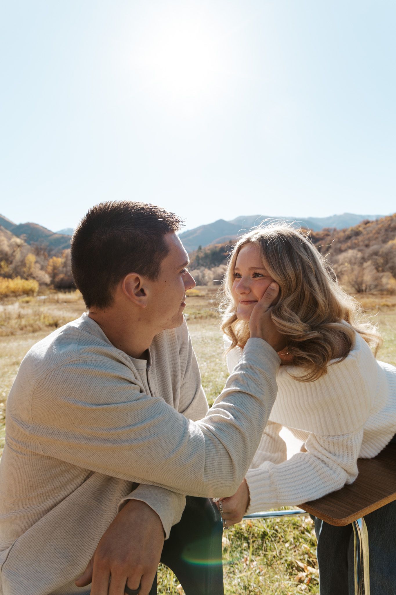 Man gently touching woman's face as they share an intimate moment outdoors in sunny mountains.