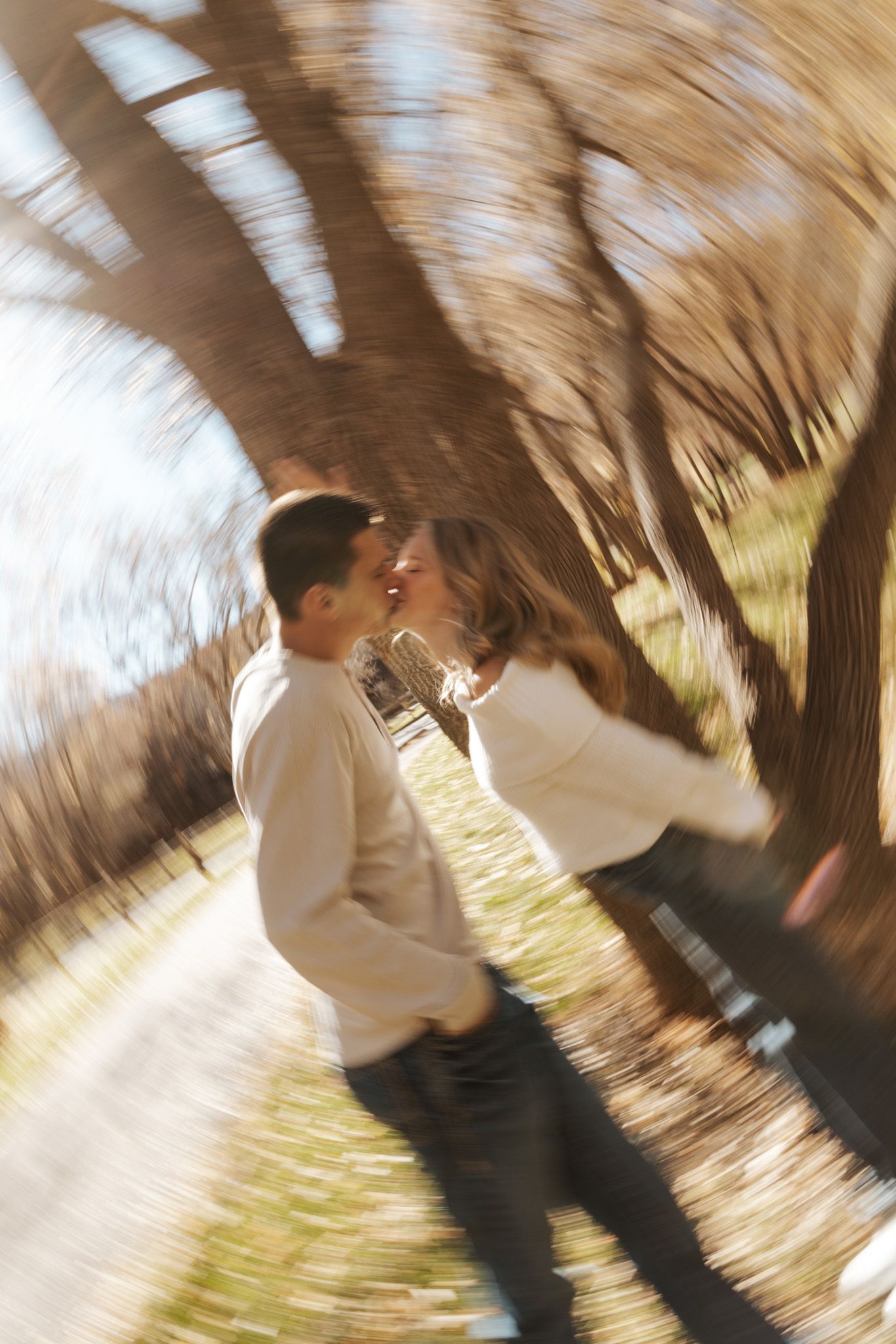 Artistic zoom-blur photo of couple almost kissing beneath trees in warm sunlight.
