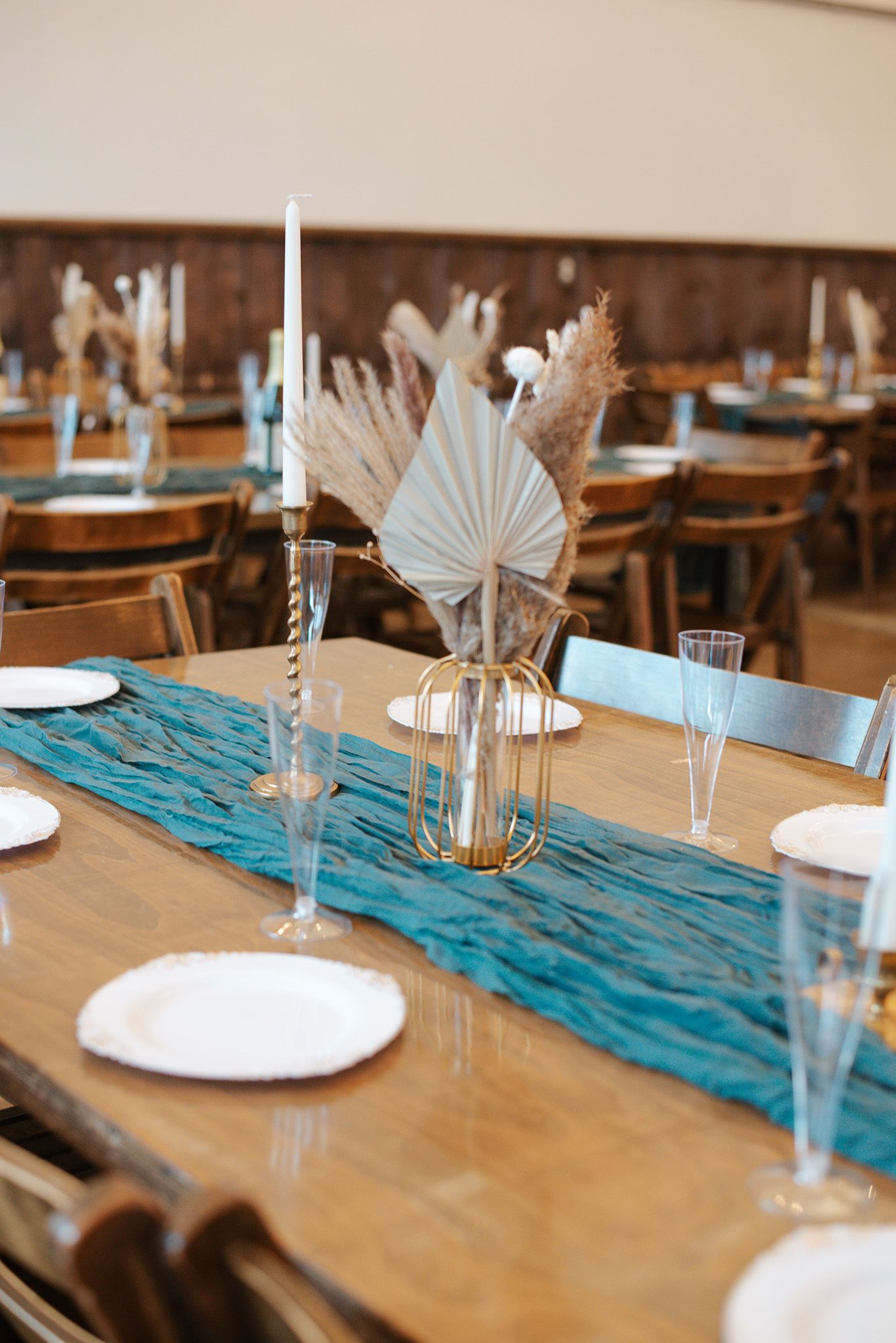 Elegant wedding reception table with teal runner, gold centerpiece, dried palms, and candles.