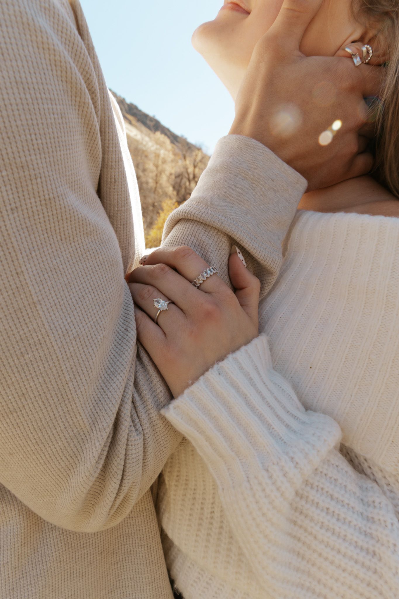 Close-up of couple holding hands, woman wearing diamond engagement ring and cream knit sweater.
