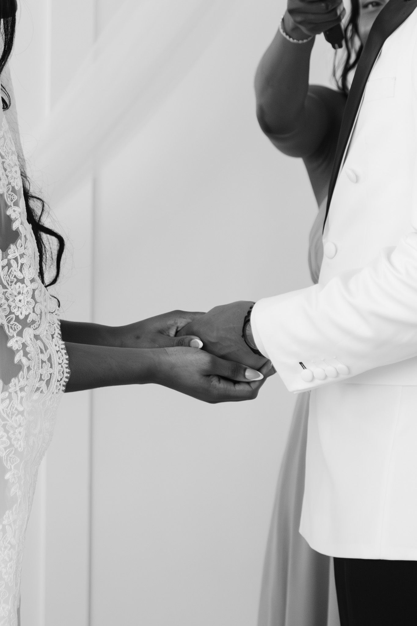 Black and white photo of bride and groom holding hands during wedding ceremony vows.
