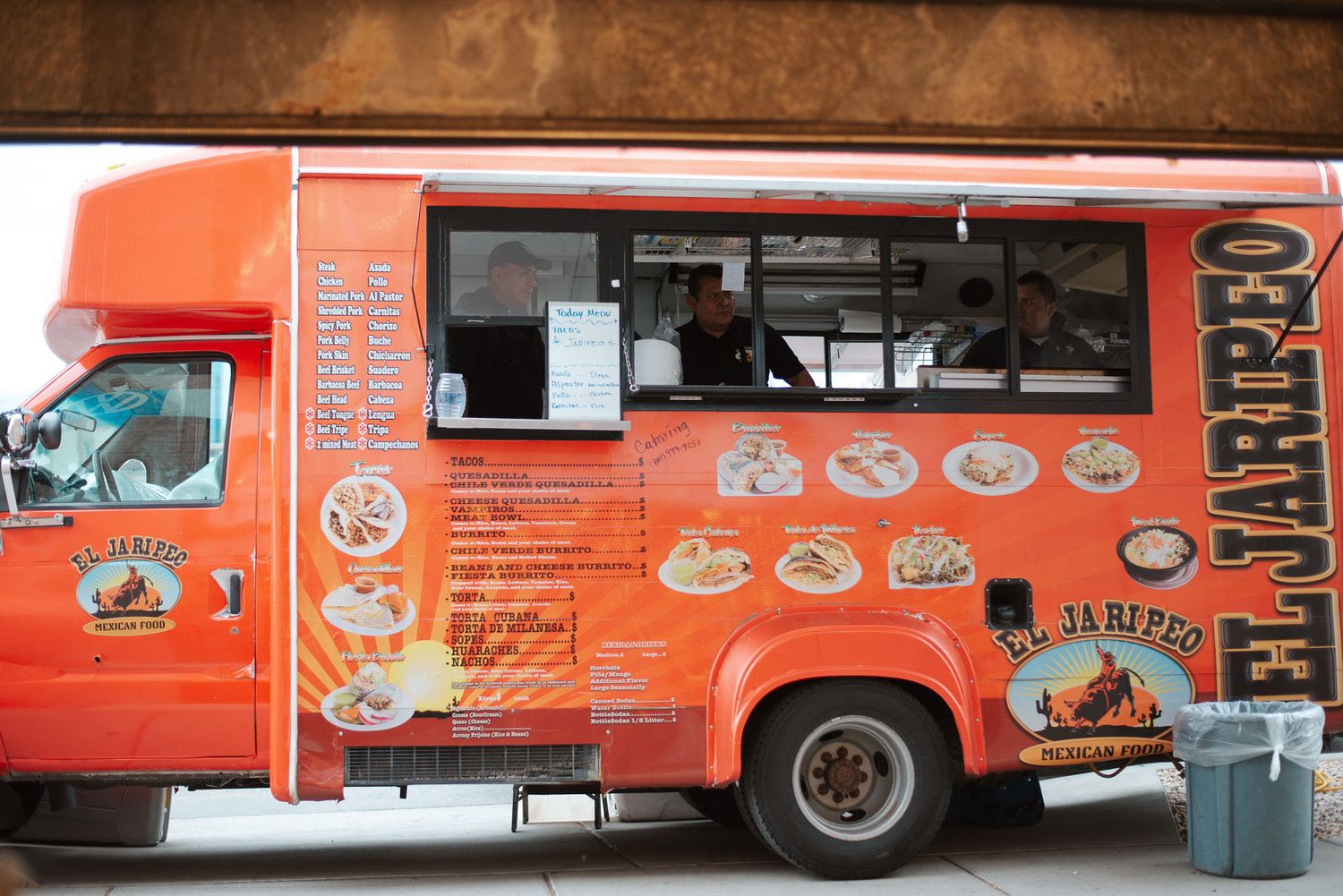 Colorful orange El Jaripeo food truck with menu graphics parked outside a building.