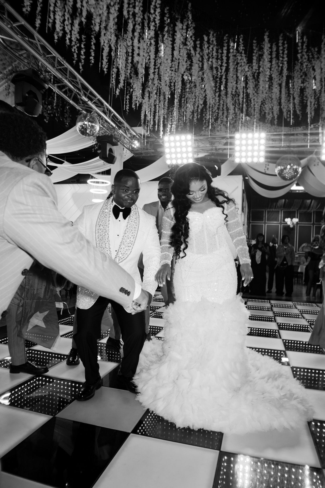 Black and white photo of a bride and groom sharing their first dance on a checkered floor at an elegant wedding reception.