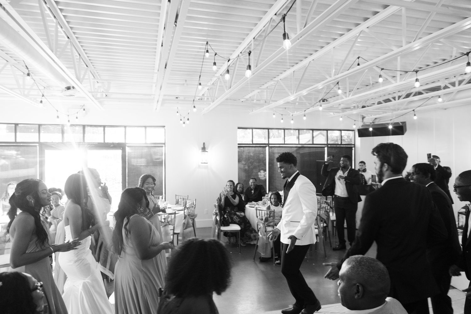 Black and white photo of wedding guests dancing at lively indoor reception celebration.