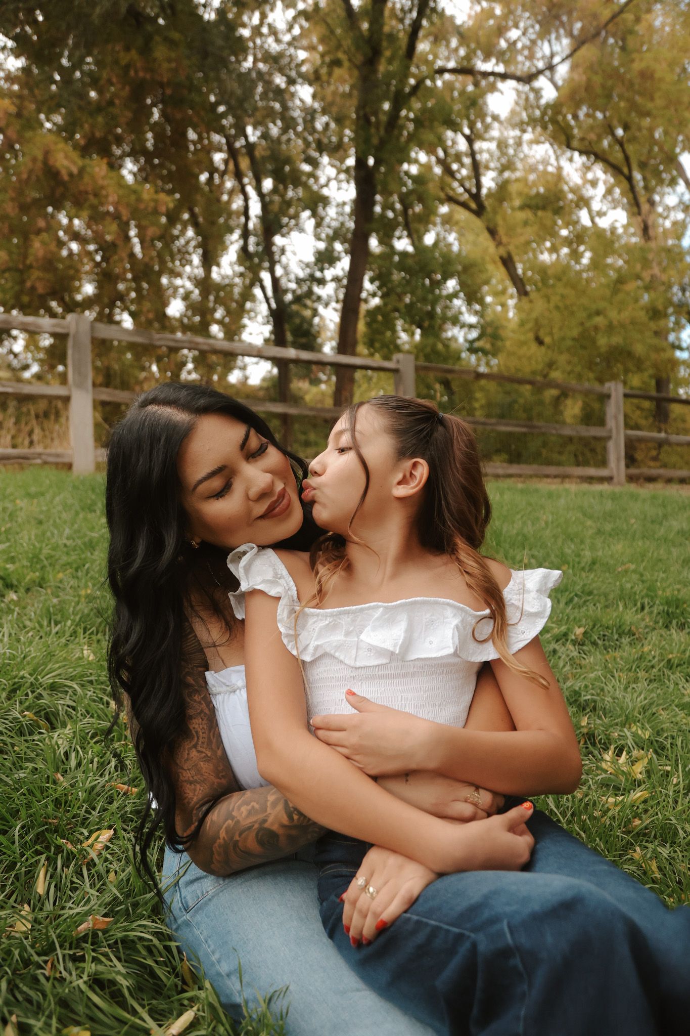 Mother and young daughter sharing a sweet kiss while sitting on green grass in an autumn park.