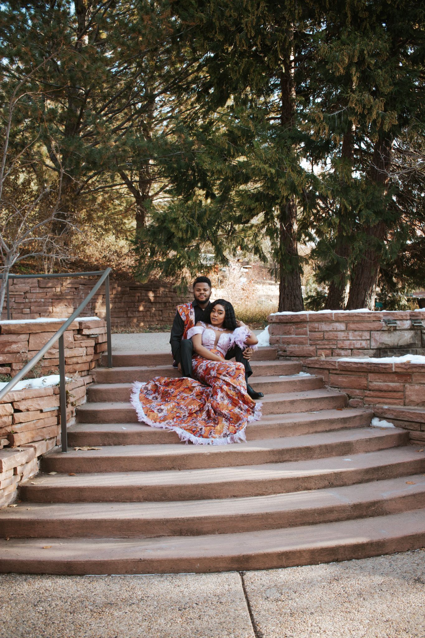 Couple posing on stone steps in a park, woman wearing a colorful traditional Mexican dress.