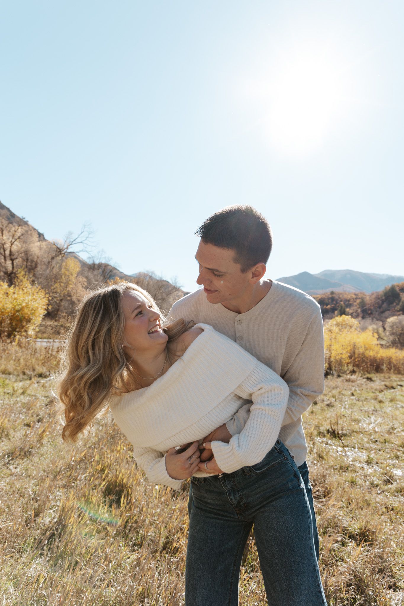 Happy couple embracing and laughing in a sunny mountain meadow with autumn foliage.