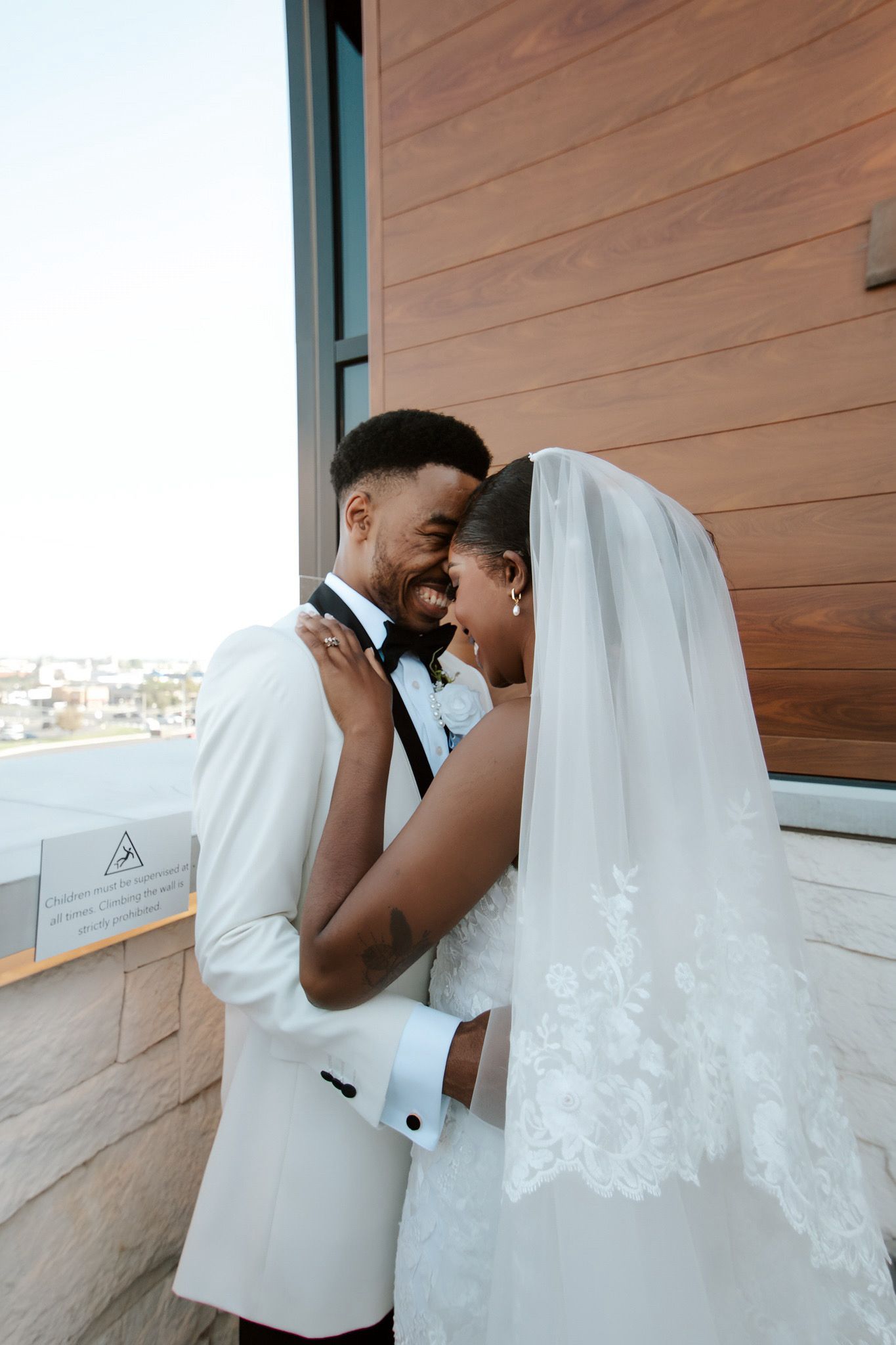 A laughing bride and groom in formal attire share an intimate moment outdoors on their wedding day.