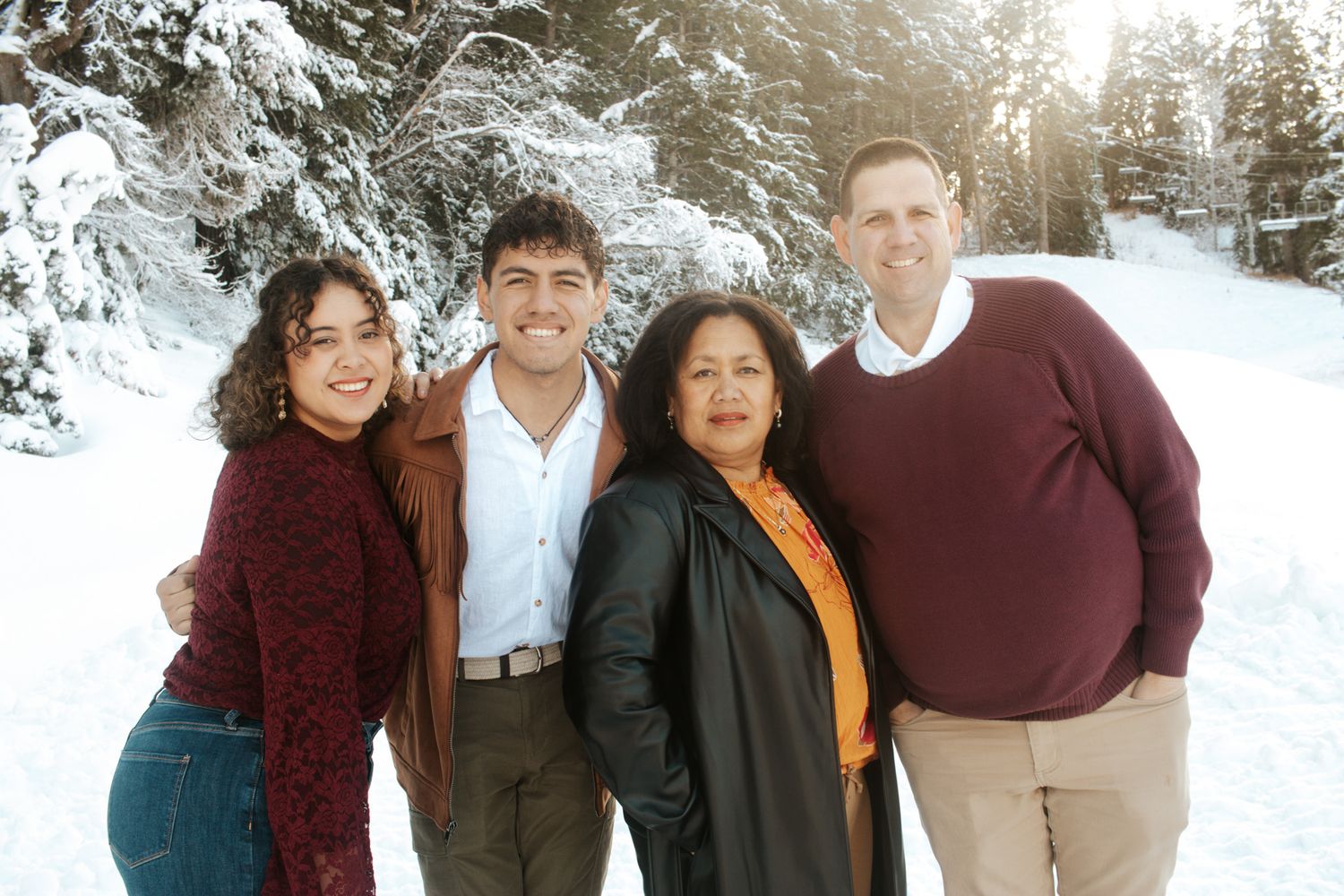 Family of four smiling together in a snowy winter forest setting for a holiday photo session.