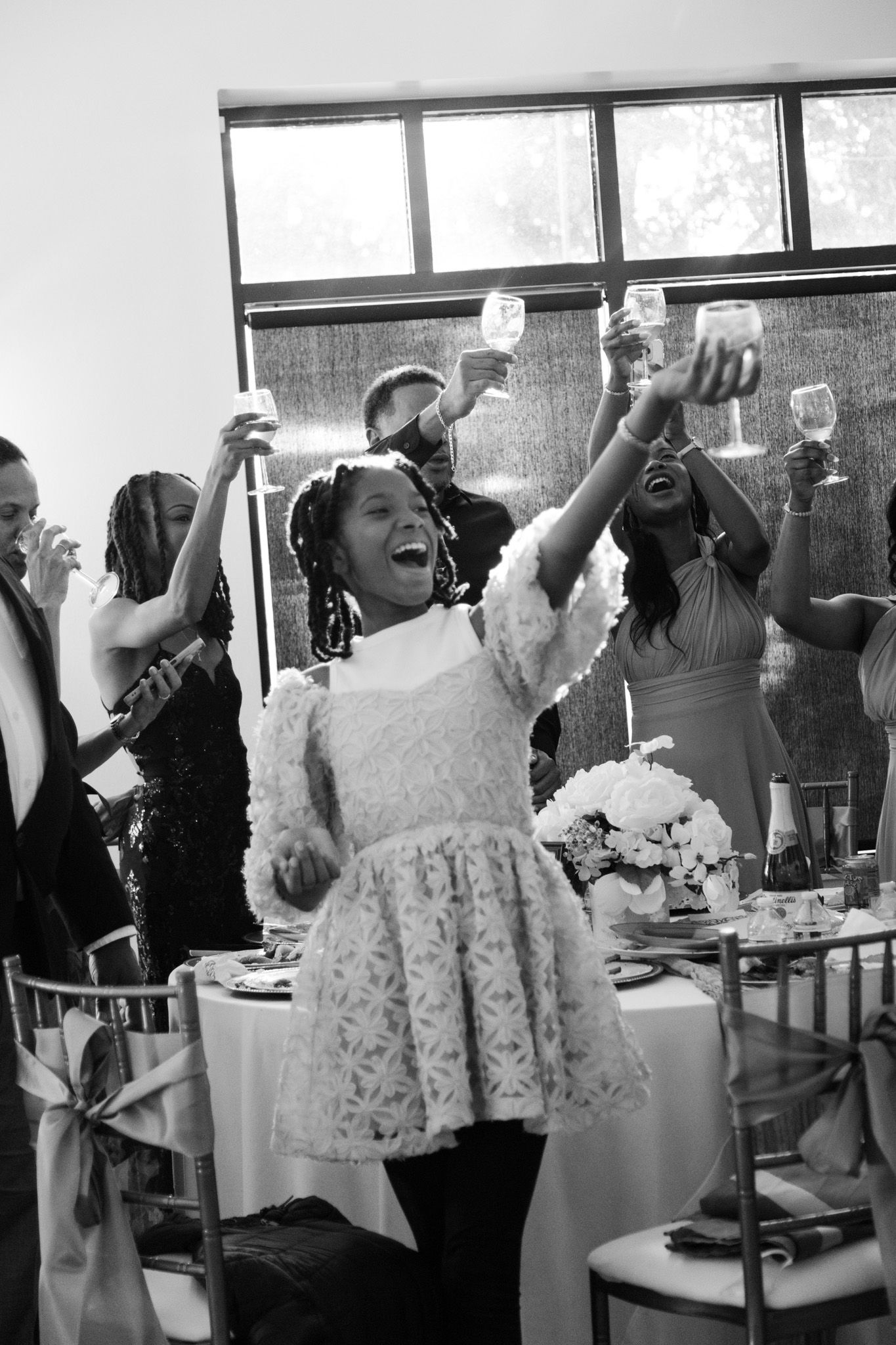 Joyful young girl raises champagne glass during wedding reception toast in black and white photo.