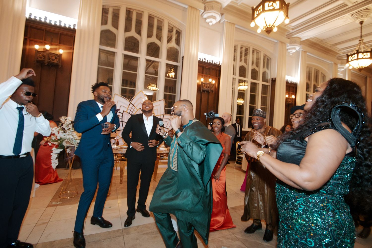 Wedding guests in formal attire dance and celebrate joyfully in elegant ballroom reception.