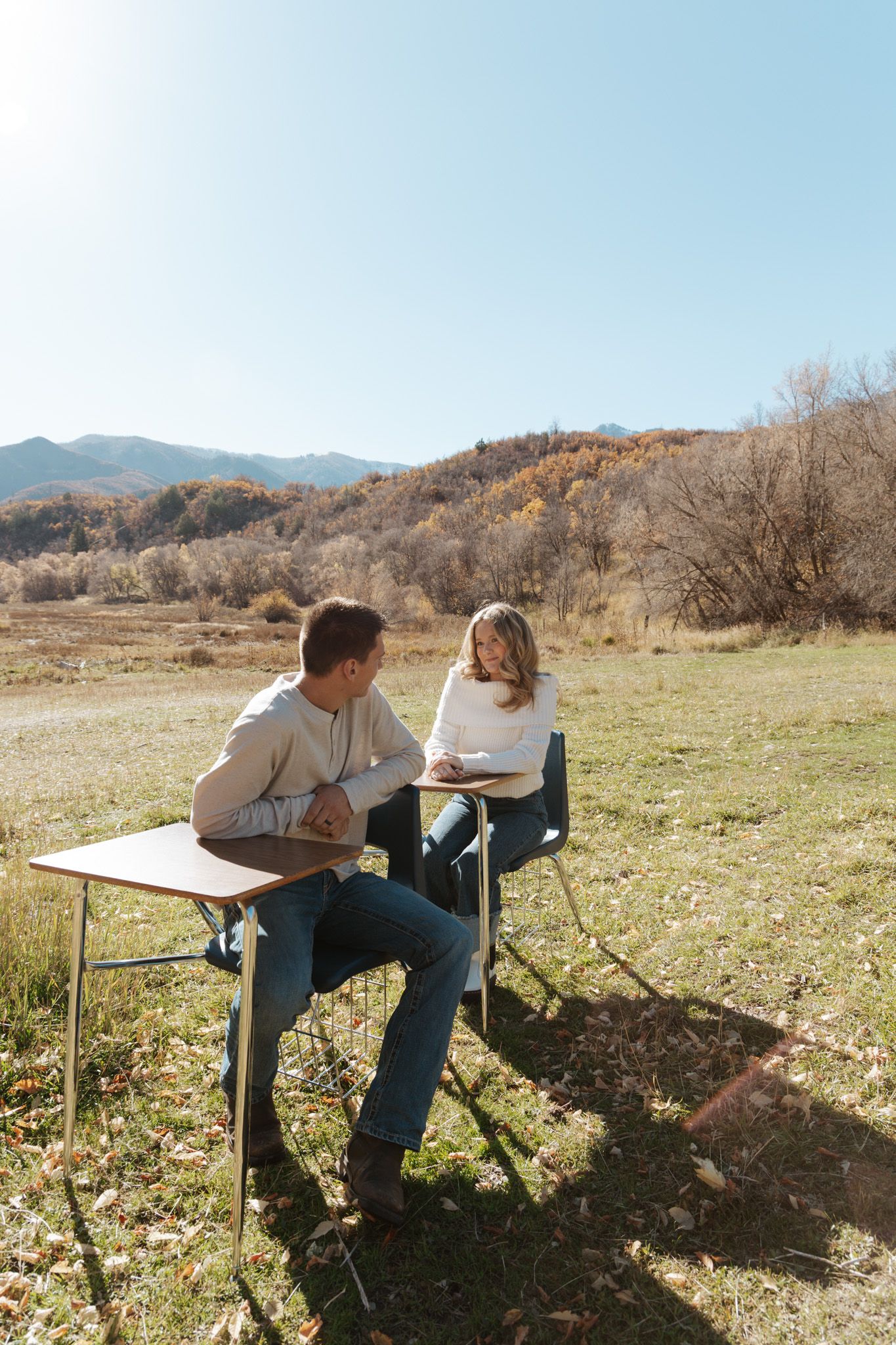 Couple sitting at school desks outdoors in an autumn mountain meadow under blue sky.