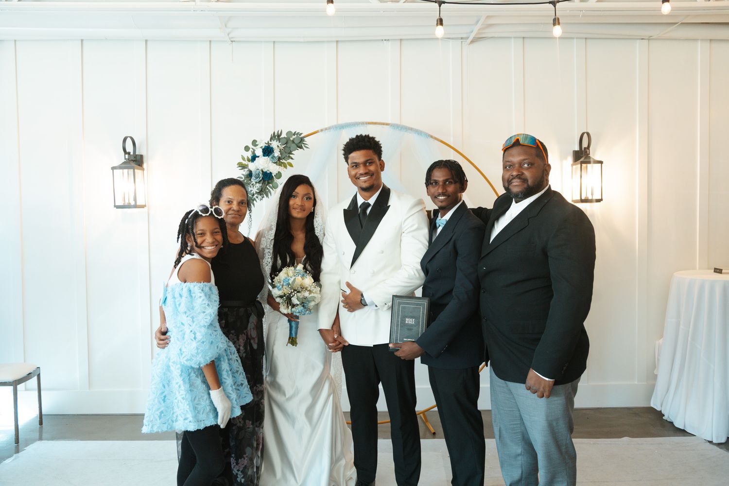 Wedding party group photo with bride and groom in front of circular floral arch backdrop.