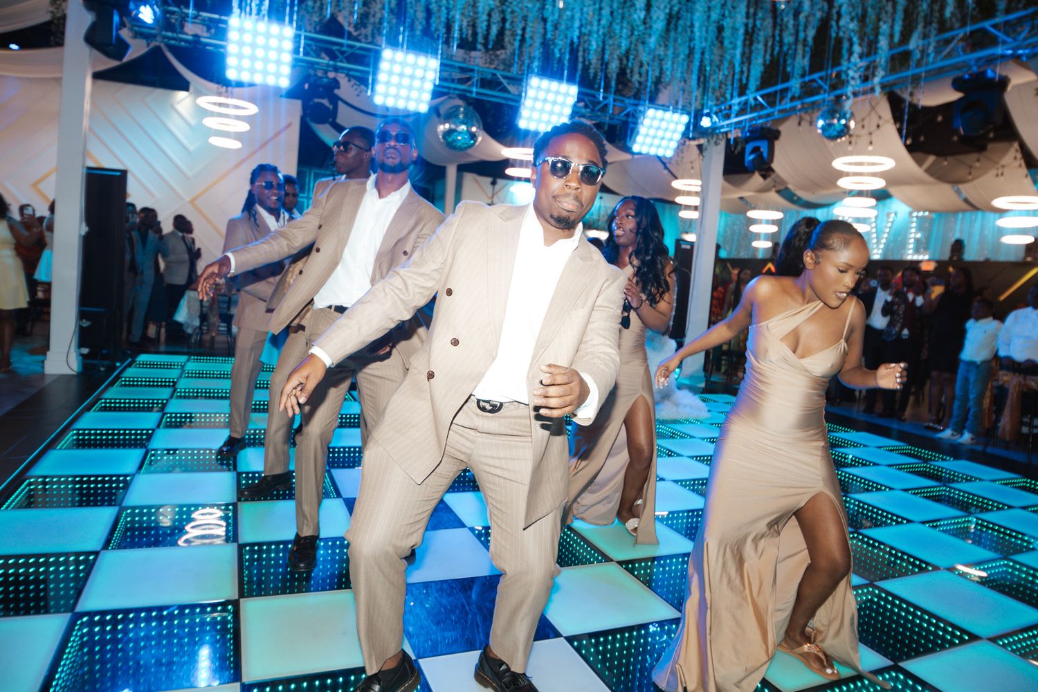 People dancing energetically on a illuminated black and white checkered dance floor at an elegant event.