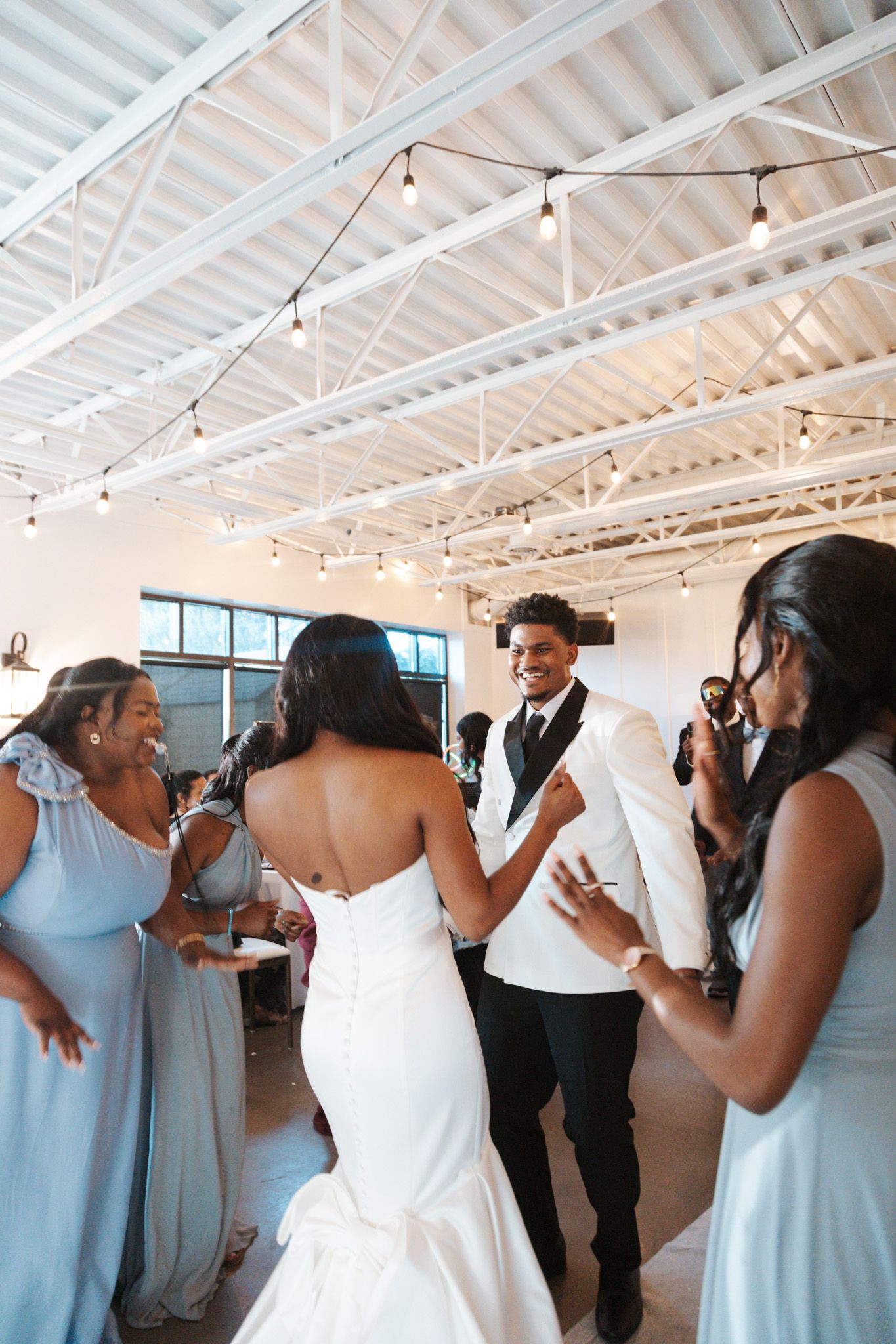 Bride and groom dancing joyfully with bridesmaids in blue dresses at wedding reception.