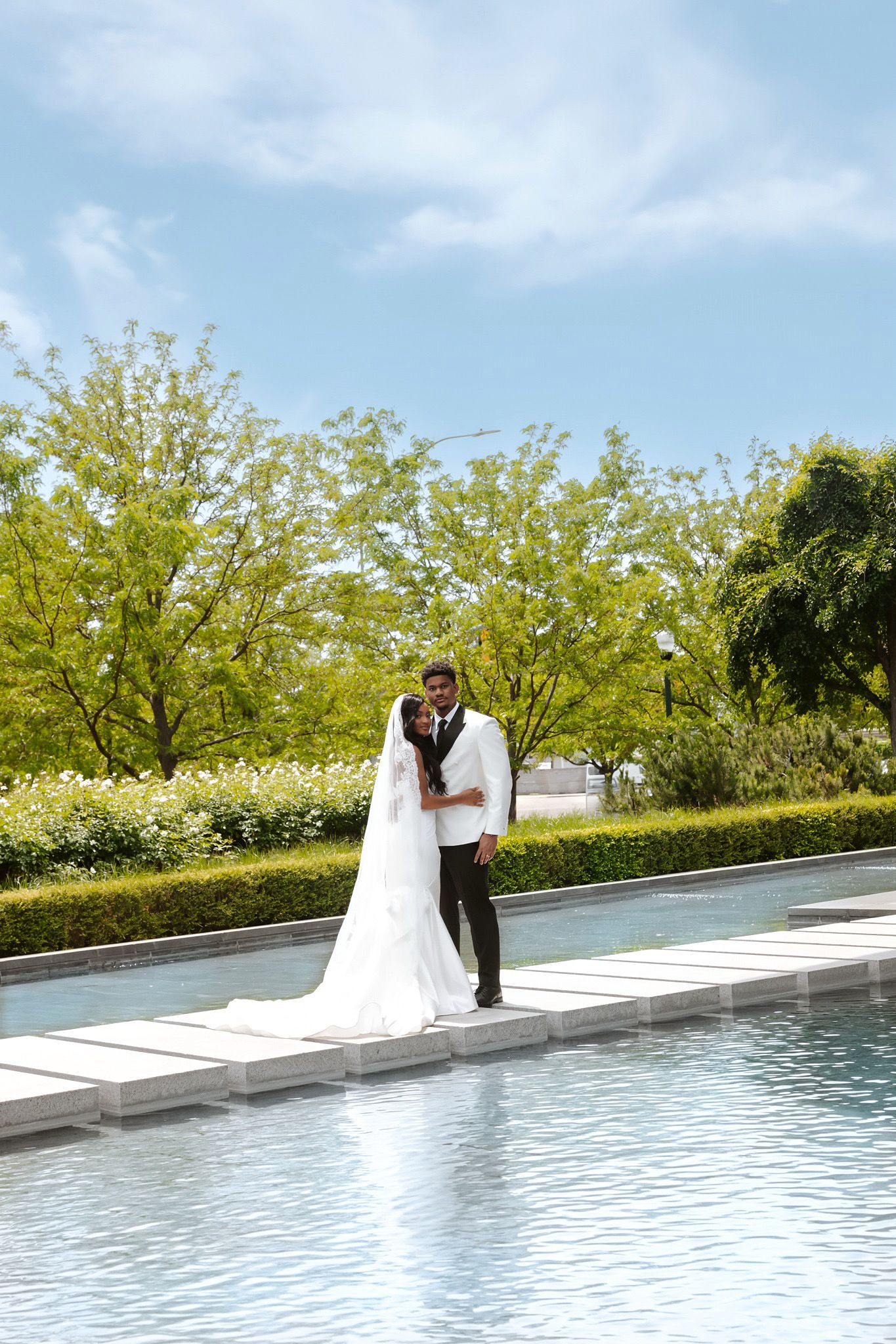 A bride and groom share a romantic moment by a reflective pool surrounded by lush greenery on their wedding day.