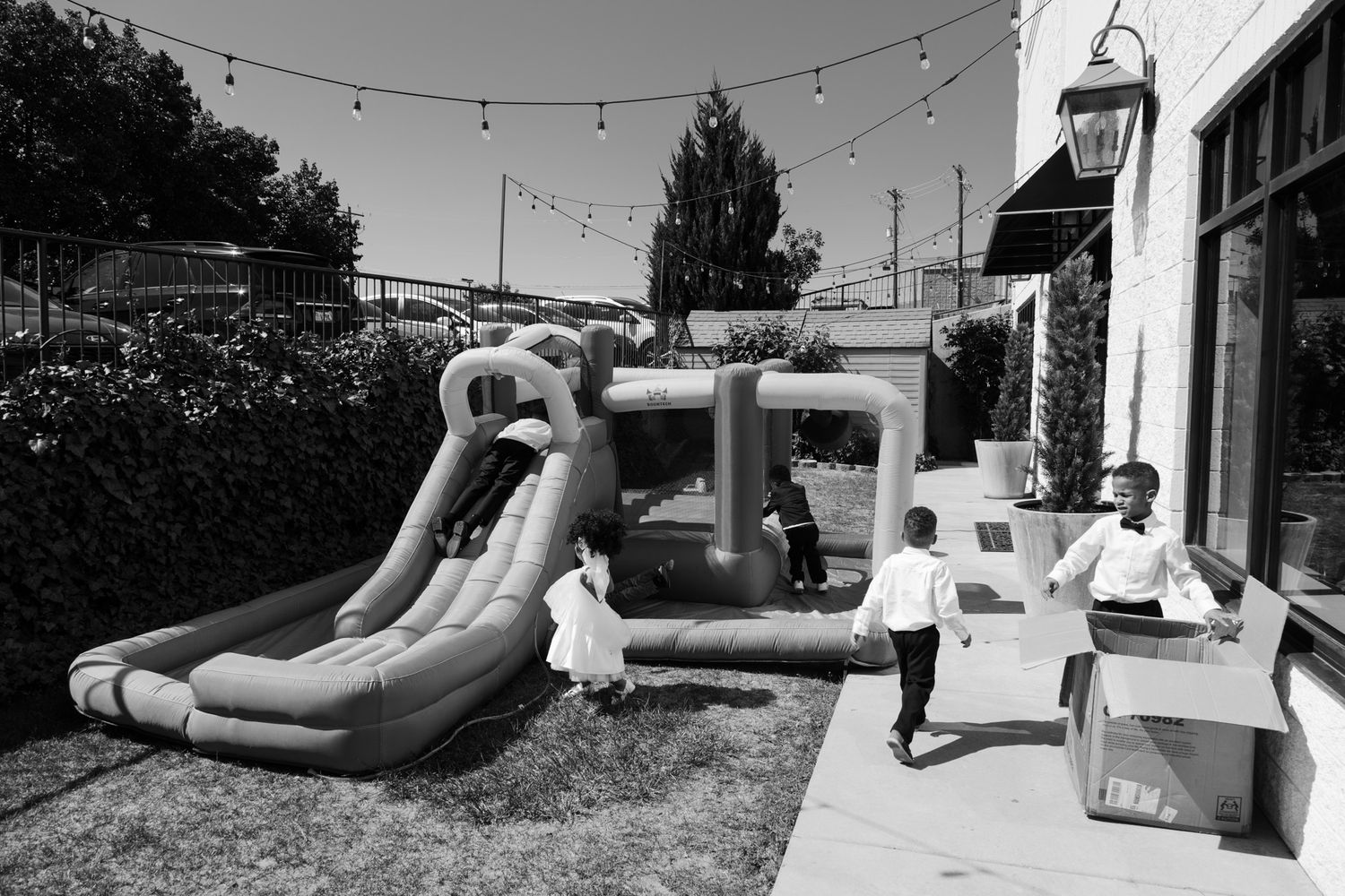 Children playing near an inflatable bounce house and slide in a backyard party setting, black and white photo.