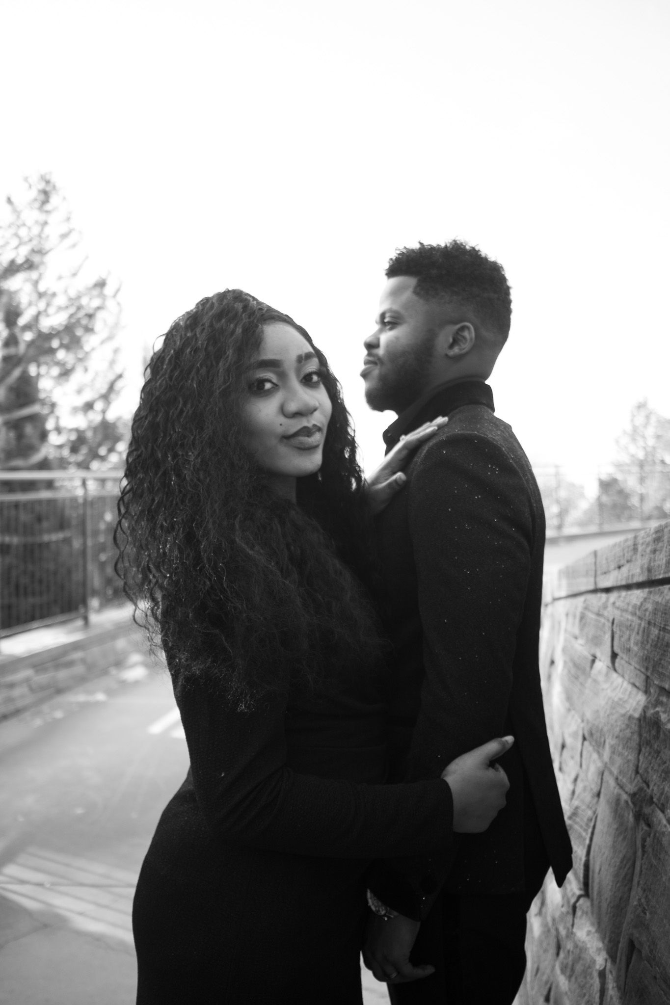 Black and white portrait of a couple embracing near a stone wall outdoors.