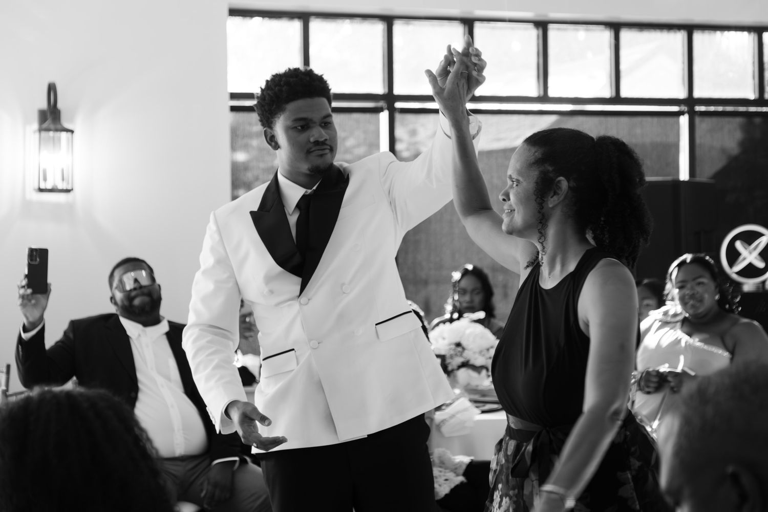 Groom in white tuxedo shares a joyful moment with a guest on the dance floor at wedding reception.
