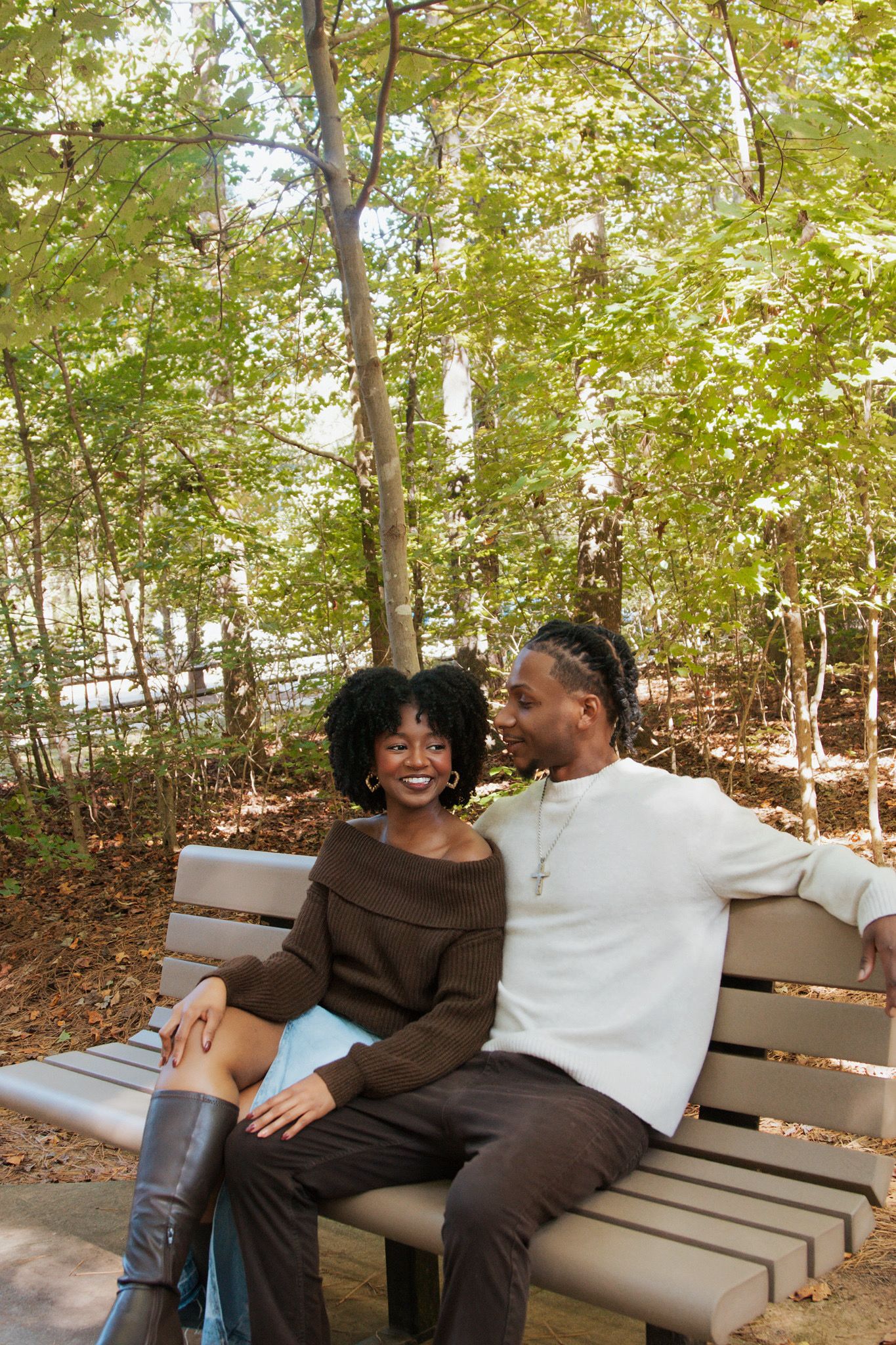 Happy couple sitting together on a park bench surrounded by lush green trees in autumn.